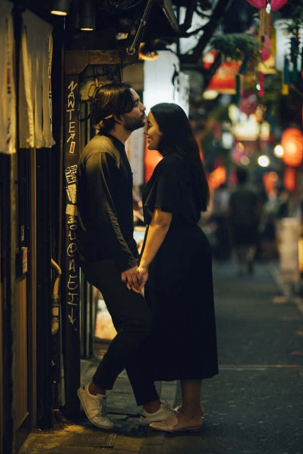 一對情侶在夜晚東京狹窄街道上牽手微笑。