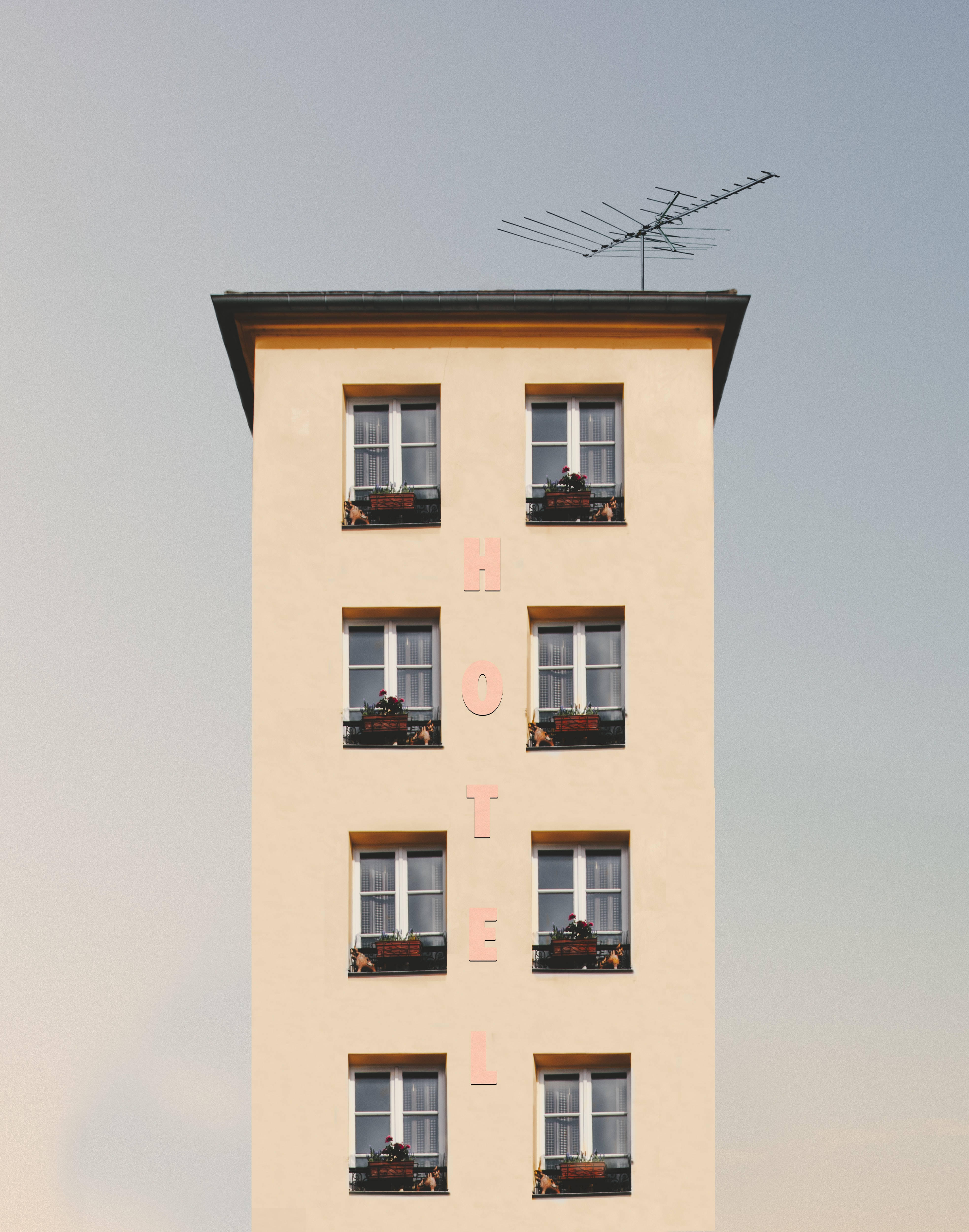 時尚酒店建築 壁紙 — 一座高大的米色酒店建築，帶有垂直的粉紅色字樣和窗台上的花箱，背景是淡色的天空。