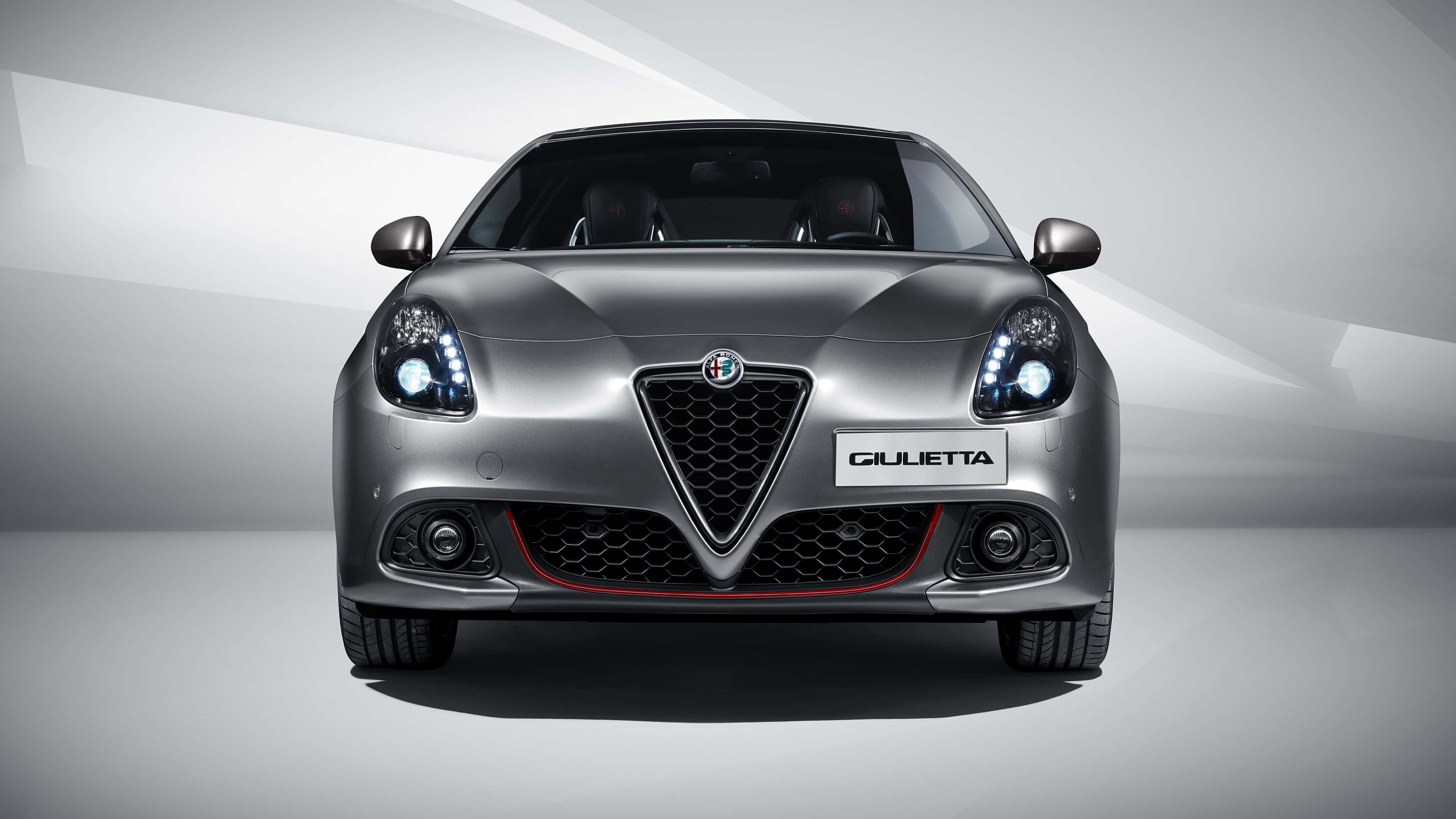 Alfa Romeo Giulietta 桌布 壁紙 — 時尚銀色 Alfa Romeo Giulietta 的前視圖，帶有發光頭燈，背景為簡約工作室背景。