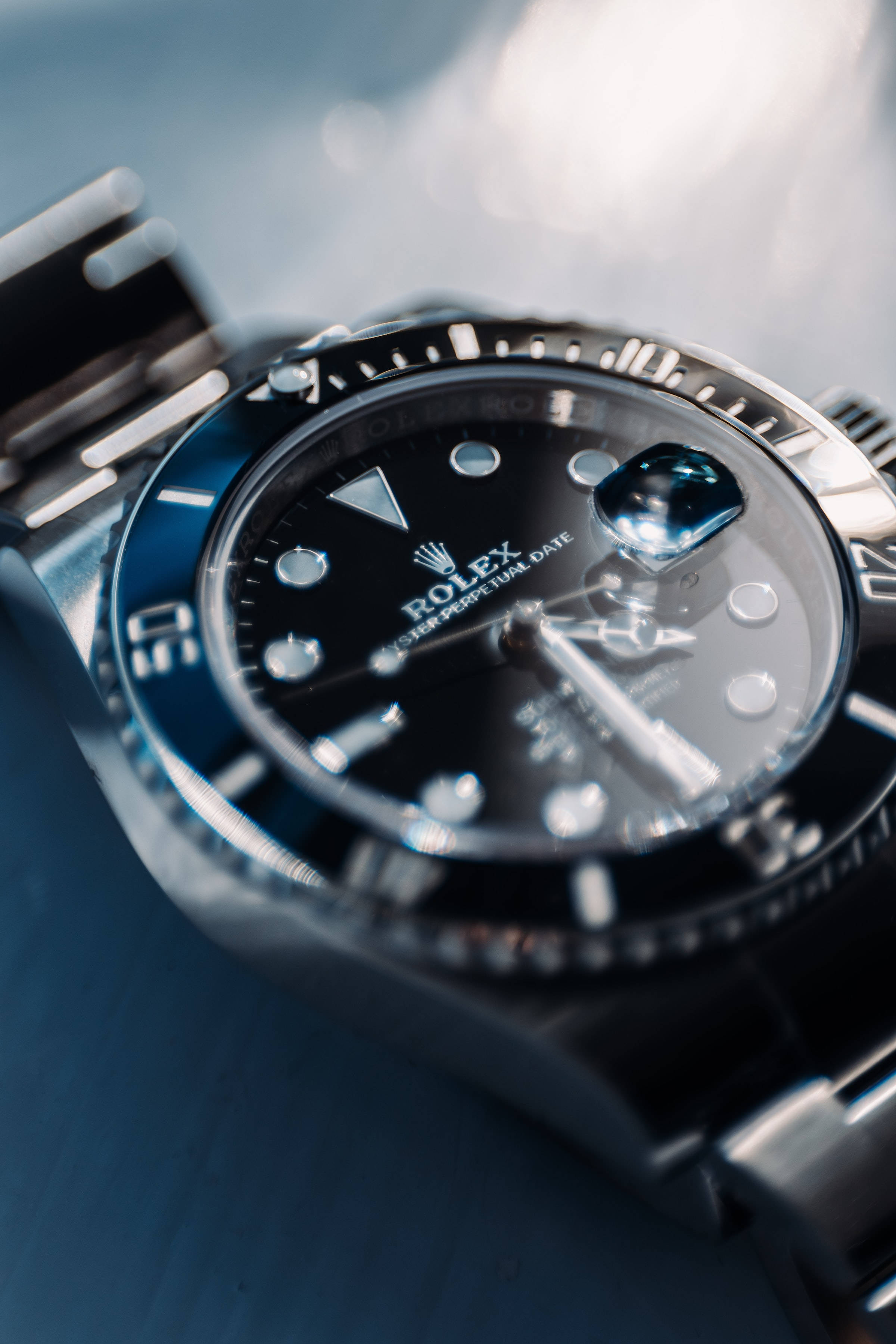 時尚銀色勞力士 壁紙 — 勞力士Submariner手錶特寫，黑色錶盤和不銹鋼錶帶，放置在帶紋理的藍色表面上。
