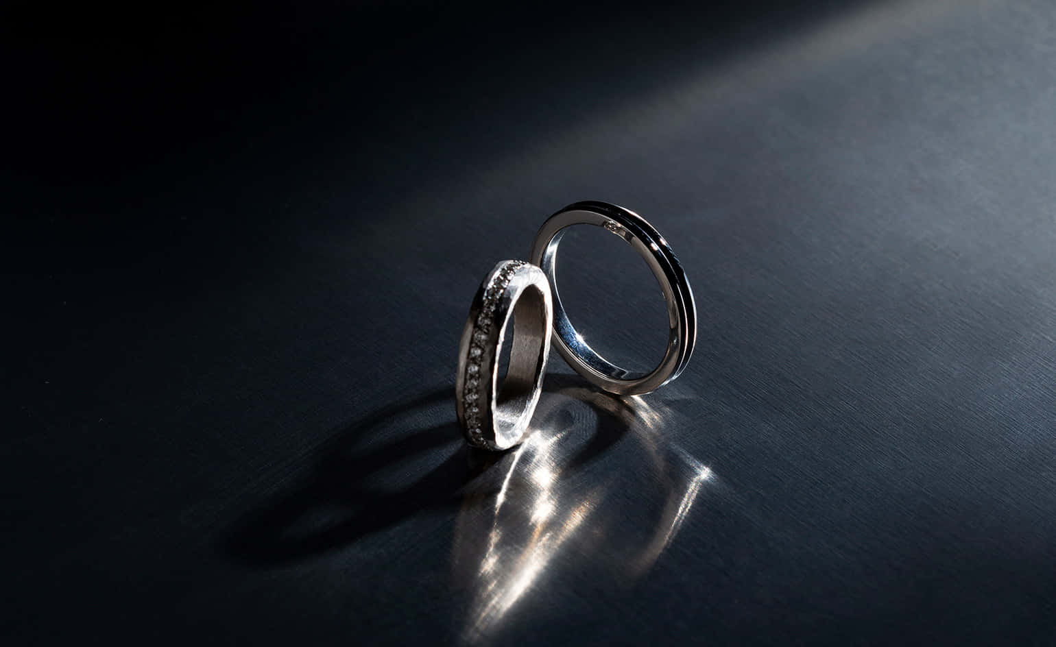 兩枚帶鑽石的結婚戒指在聚光燈下於黑暗表面上發光。