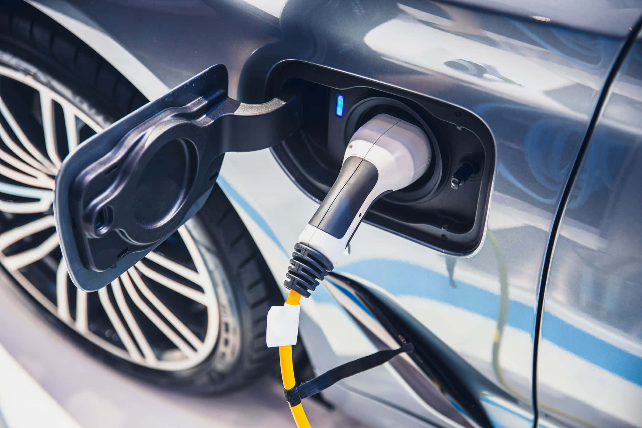 Electric Vehicle 桌布 壁紙 — 時尚電動車充電特寫，一條亮黃色電纜插入其端口。