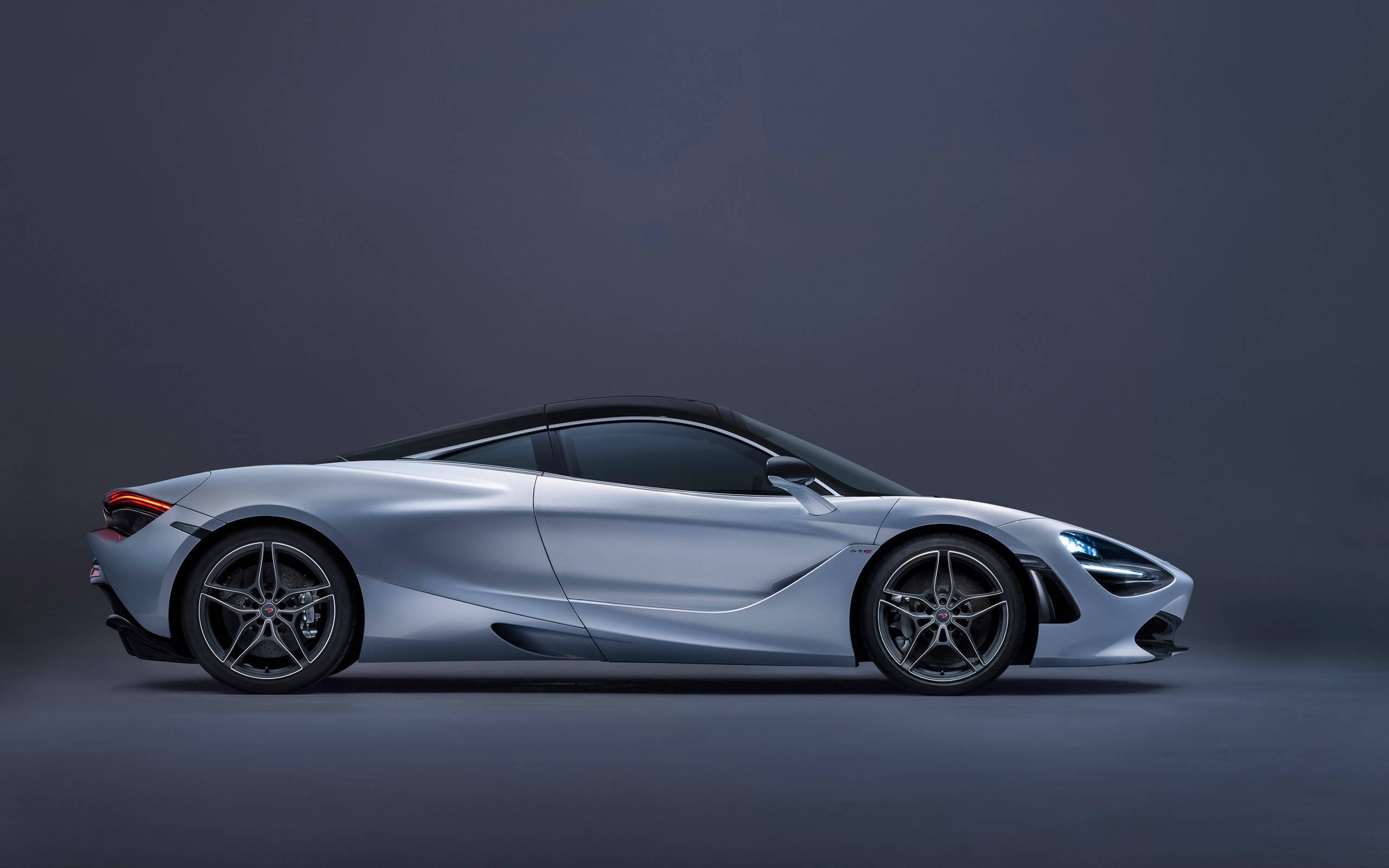 時尚麥拉倫720s 4K 壁紙 — 一輛時尚的銀色跑車，帶有發光的頭燈和尾燈，站在一個極簡主義的工作室中，背景是深灰色。