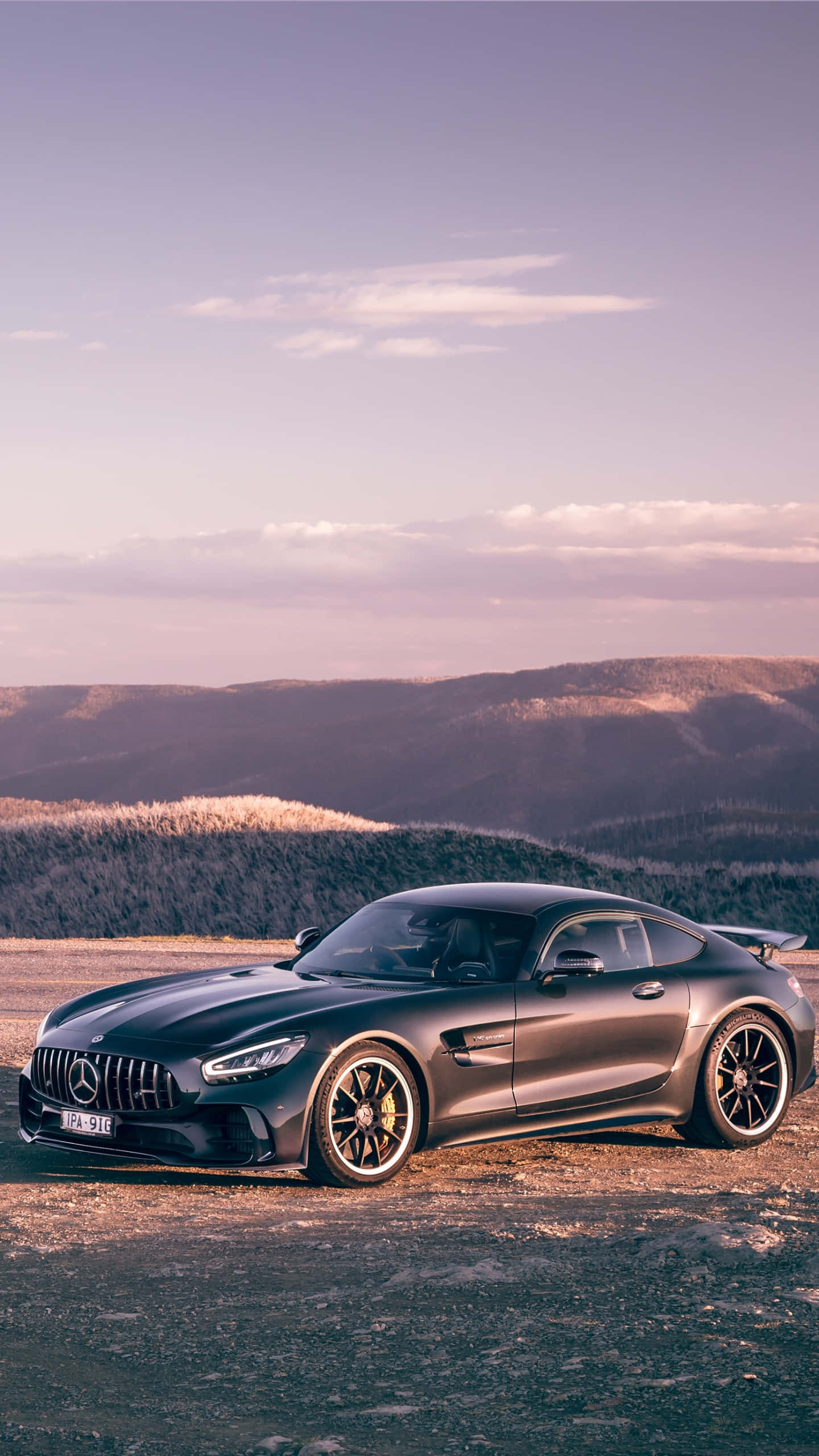 時尚黑色 Android AMG GT-R 背景 壁紙 — 一輛時尚的啞光黑色 Mercedes-AMG GT 停在日落時分的山頂觀景點，背景是連綿起伏的山丘。