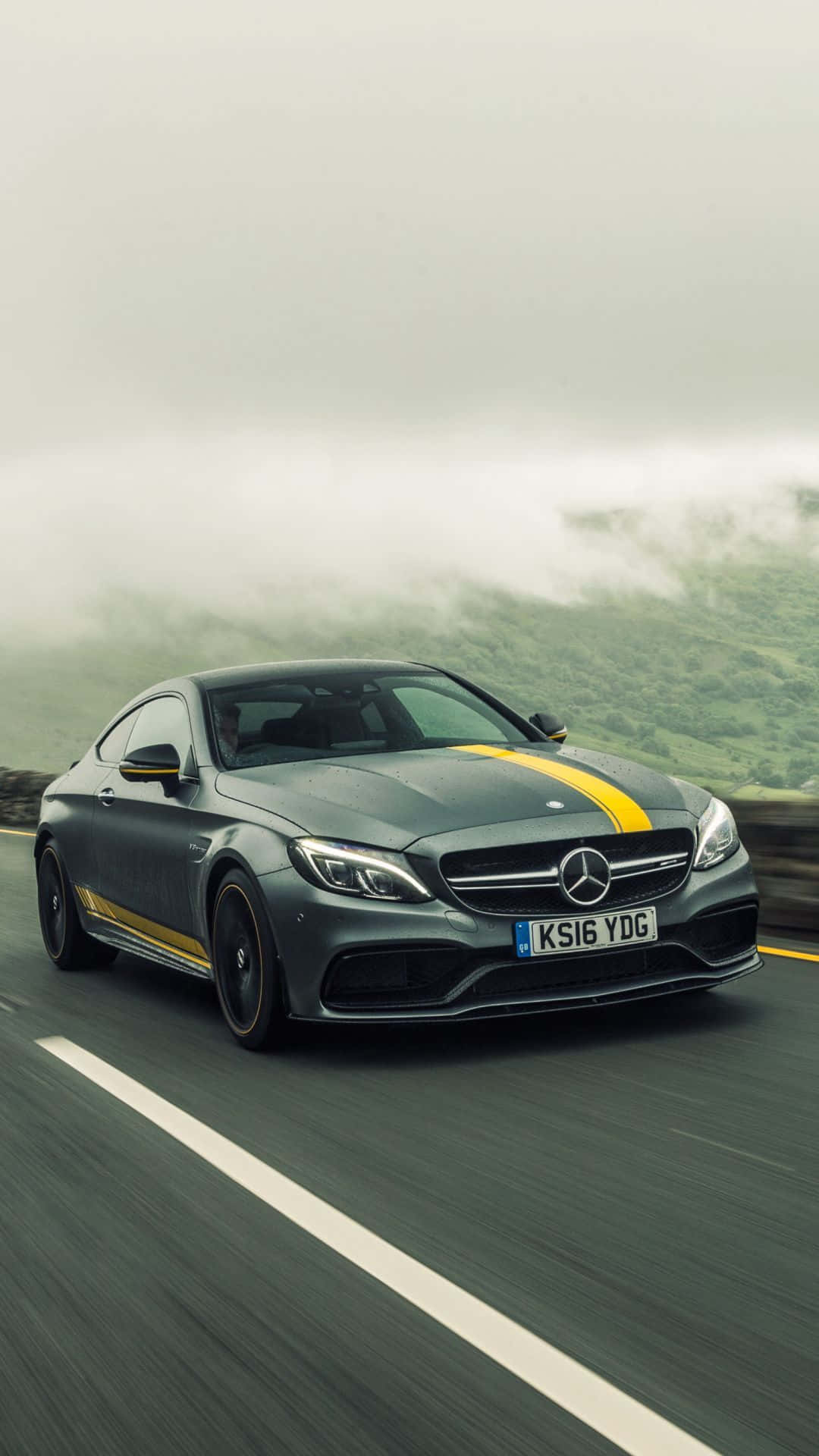灰色Mercedes-AMG C63 Coupe帶有黃色條紋，在霧氣瀰漫的山路上行駛。