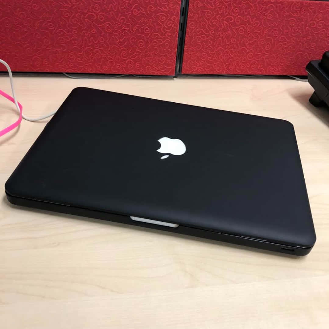關閉的黑色MacBook在木桌上，後面有紅色圖案牆板。