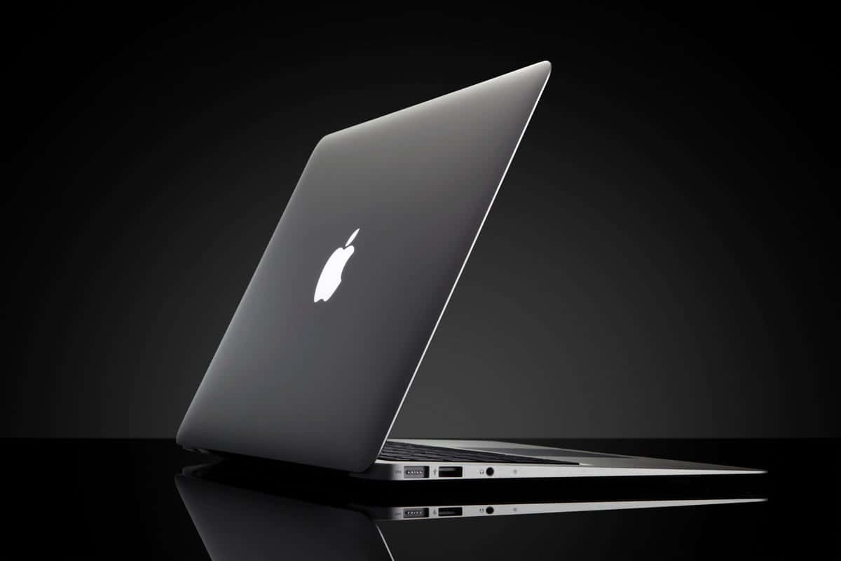 在暗色工作室燈光下，反射黑色表面上的時尚銀色 MacBook 筆記型電腦。