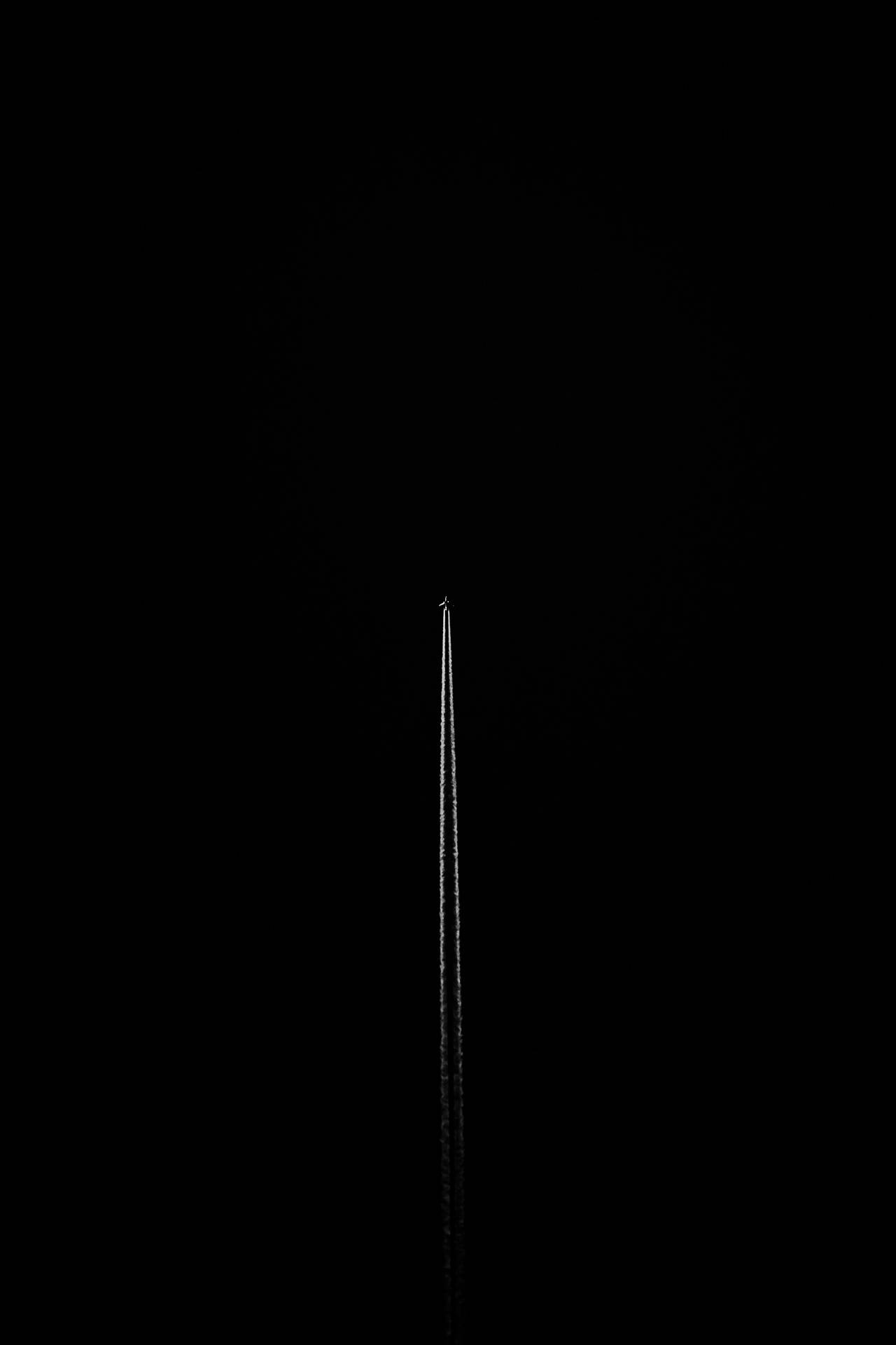 一架飛機在夜間飛行，在黑暗的天空中留下一道白色的凝結尾跡。