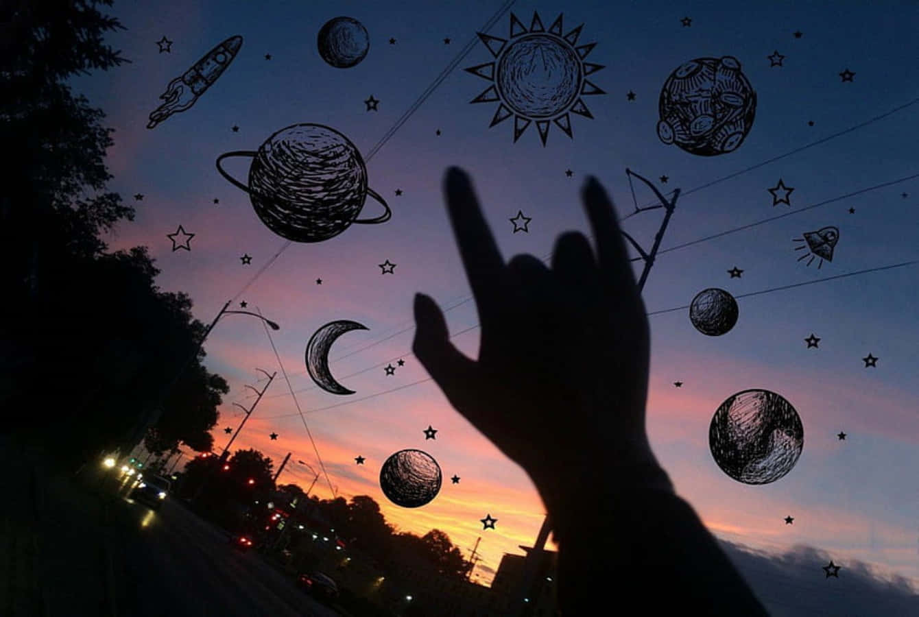 時尚龐克風格桌面宇宙行星 壁紙 — 一隻手在暮色天空的襯托下形成剪影，天空點綴著手繪的行星、星星和火箭。