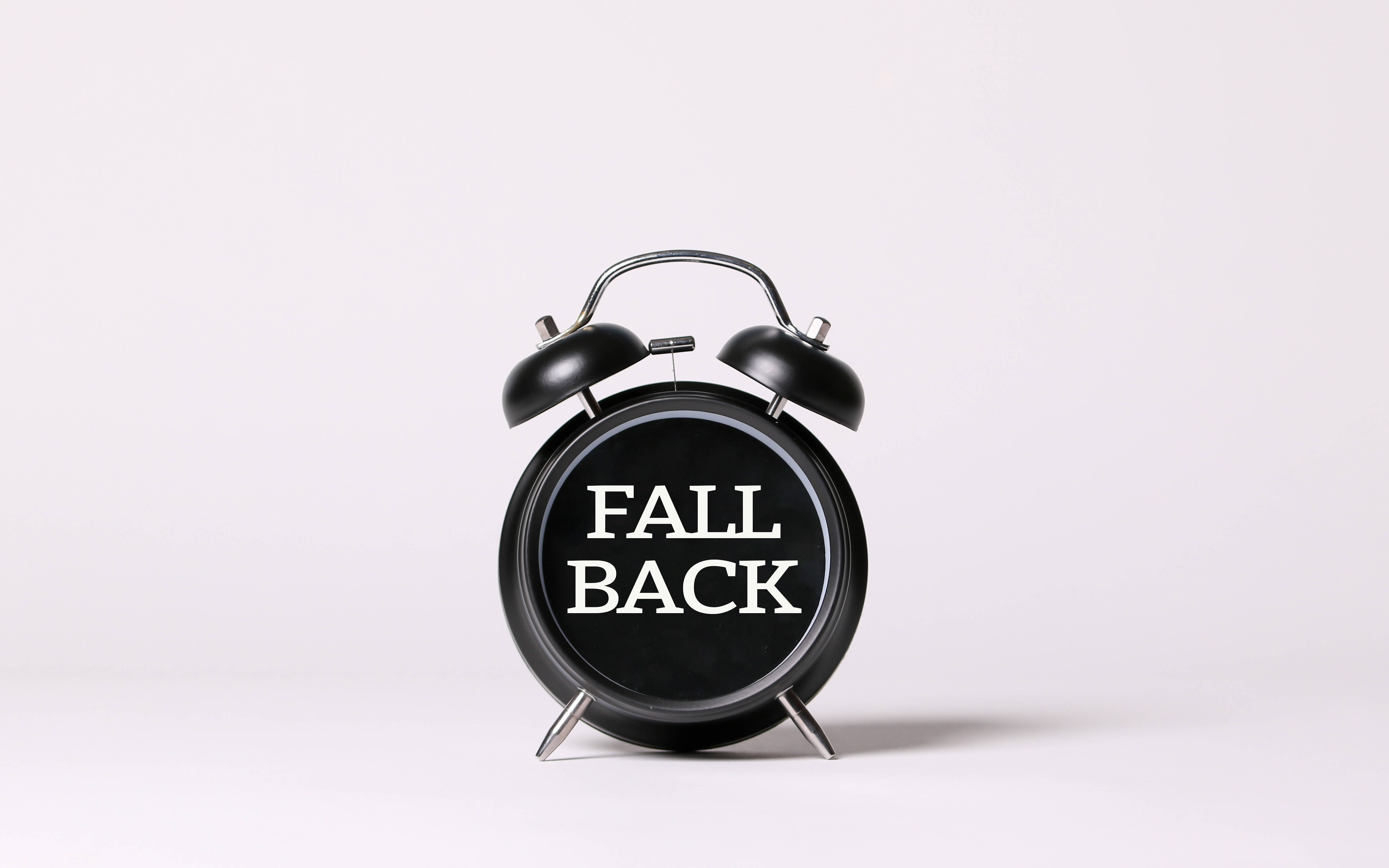 時鐘圖形設計 壁紙 — 一個黑色復古鬧鐘，上面有「FALL BACK」字樣，置於純白色背景中央。