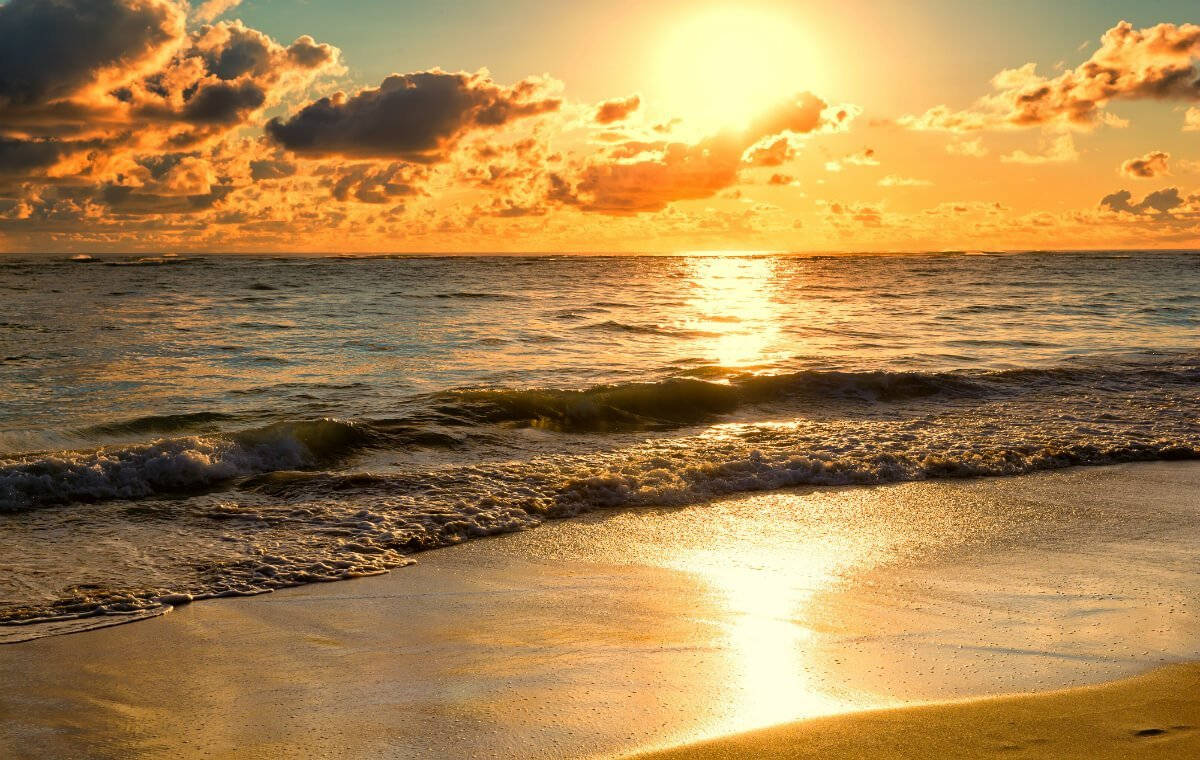 晨 glory 環繞壯麗海洋 壁紙 — 金色夕陽將溫暖光線投射在海洋波浪上，波浪伴隨著散落的雲朵湧上沙灘。