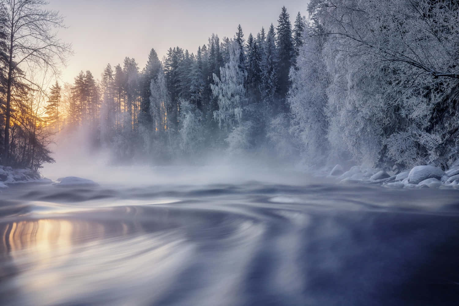 晨曦中的冰凍風景 壁紙 — 一條霧氣瀰漫的冬日河流流過積雪覆蓋的樹木，金色的日出光線穿過森林。