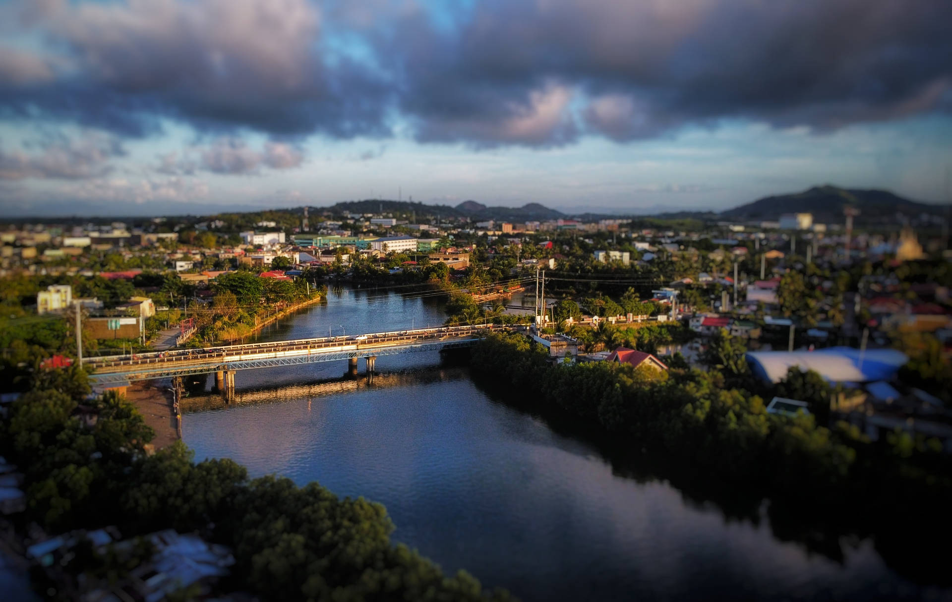晨間城市最長大橋 壁紙 — 黃昏時分河流橋樑的鳥瞰圖，帶有戲劇性的雲彩和沿岸色彩繽紛的建築物。