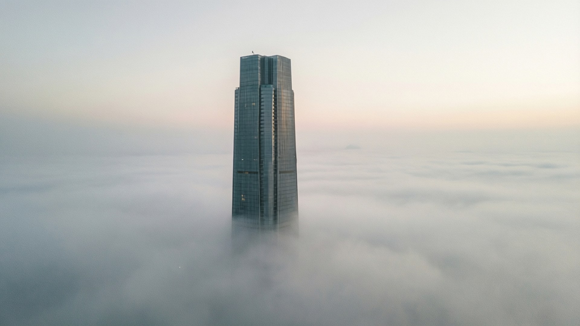 黎明時分，一座高聳的玻璃摩天大樓聳立於雲海之上