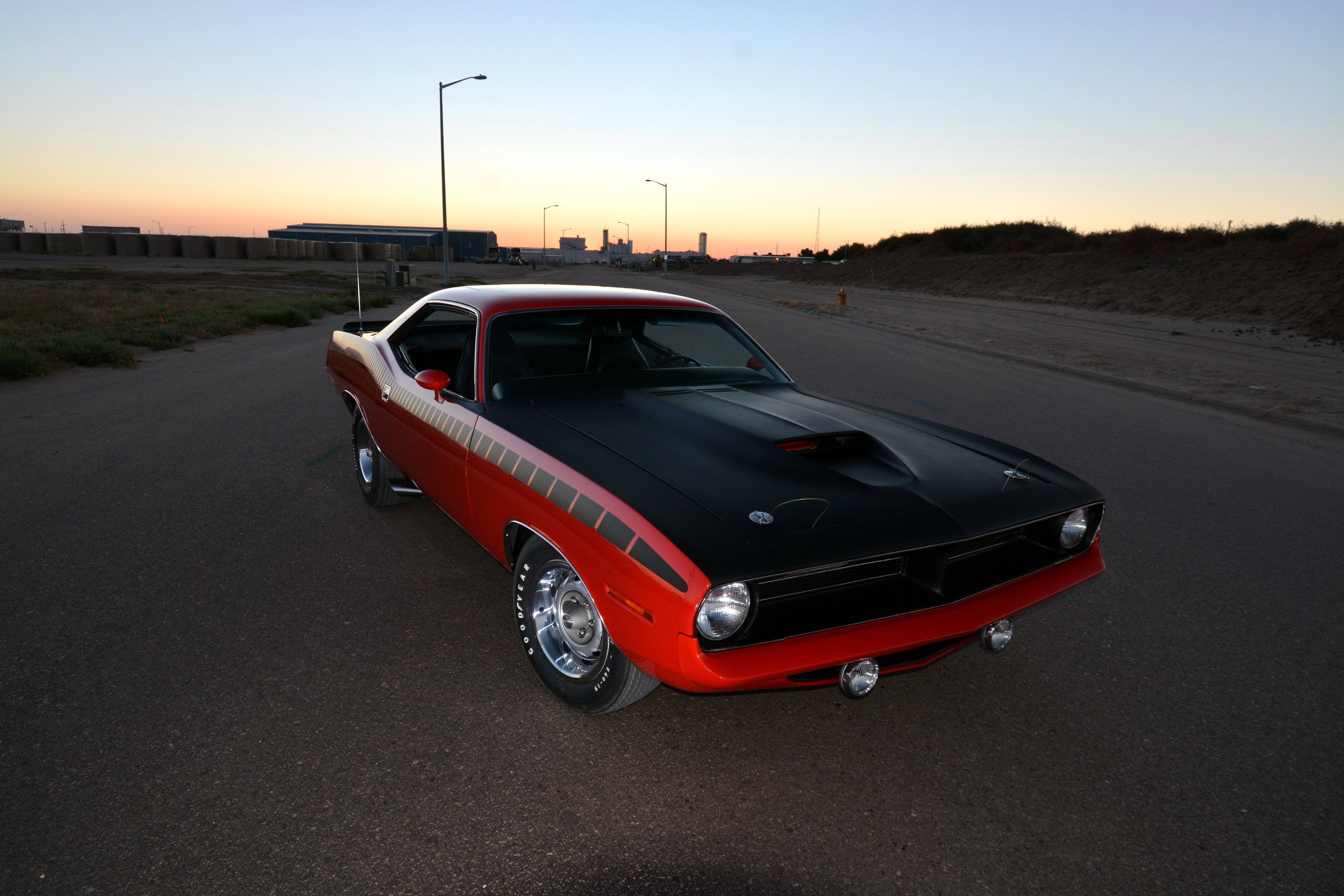普利茅斯 Barracuda 426 Hemi 壁紙 — 一輛經典紅黑色肌肉車在日落時分停泊在空曠的道路上，遠處有工業建築。