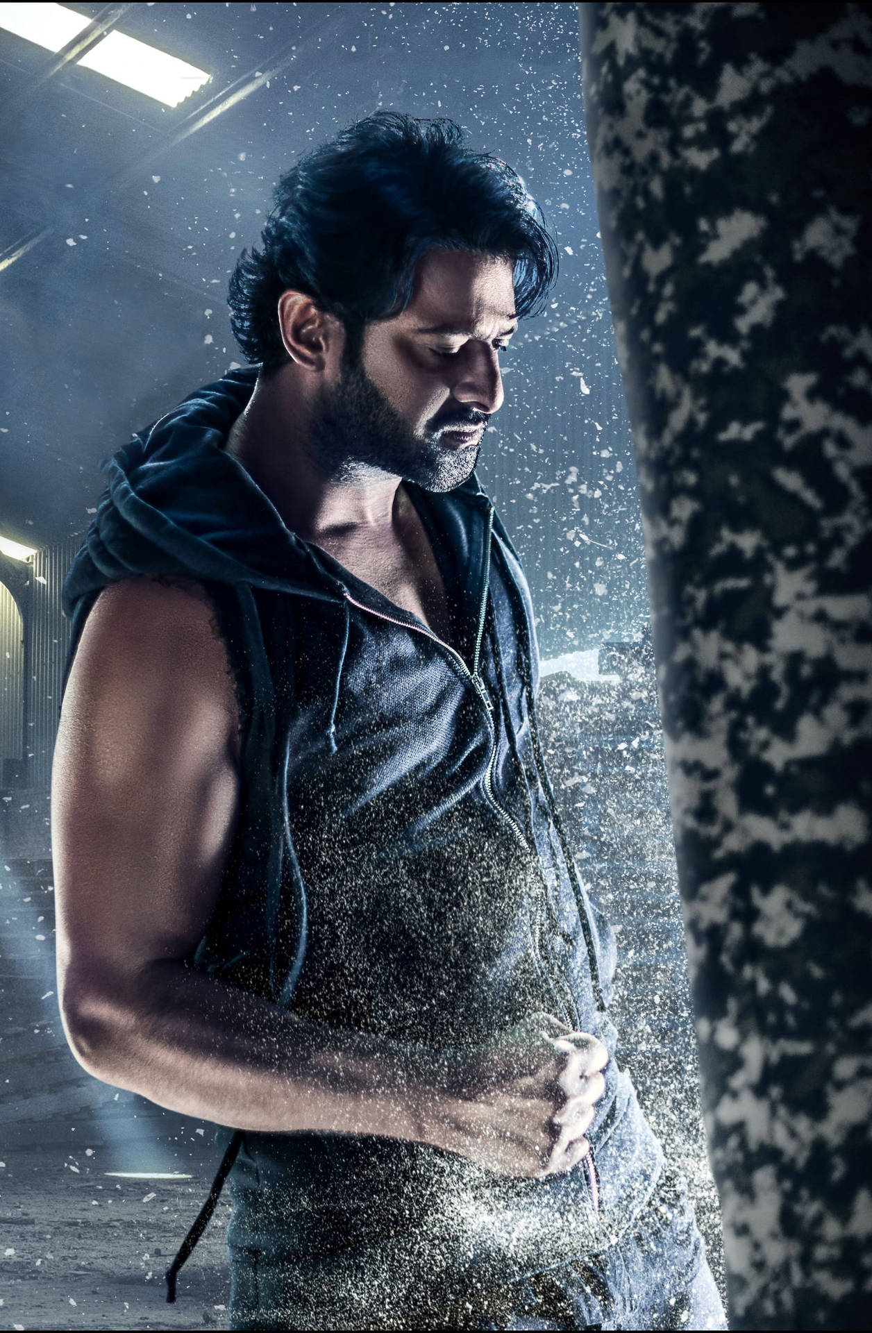一個肌肉發達的男人穿著深色連帽衫，站在粗糙的工業空間中，水花四濺。
