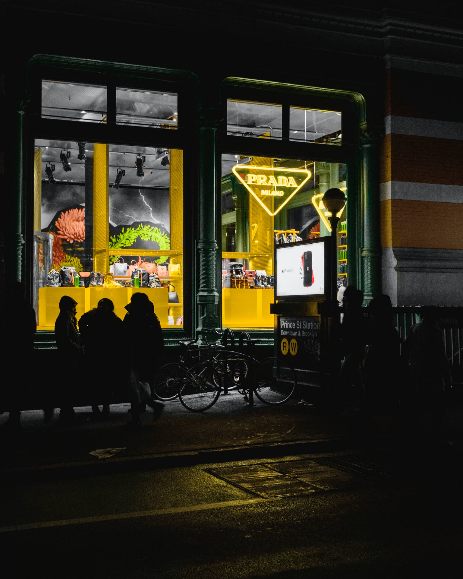 夜晚在燈光明亮的 Prada 商店外的人和自行車剪影。