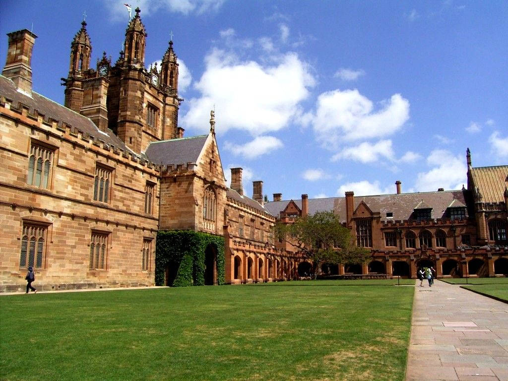 普林斯頓大學四角廣場 壁紙 — 宏偉的砂岩大學建築，哥德式塔樓聳立在修剪整齊的草坪上，上方是藍天白雲。