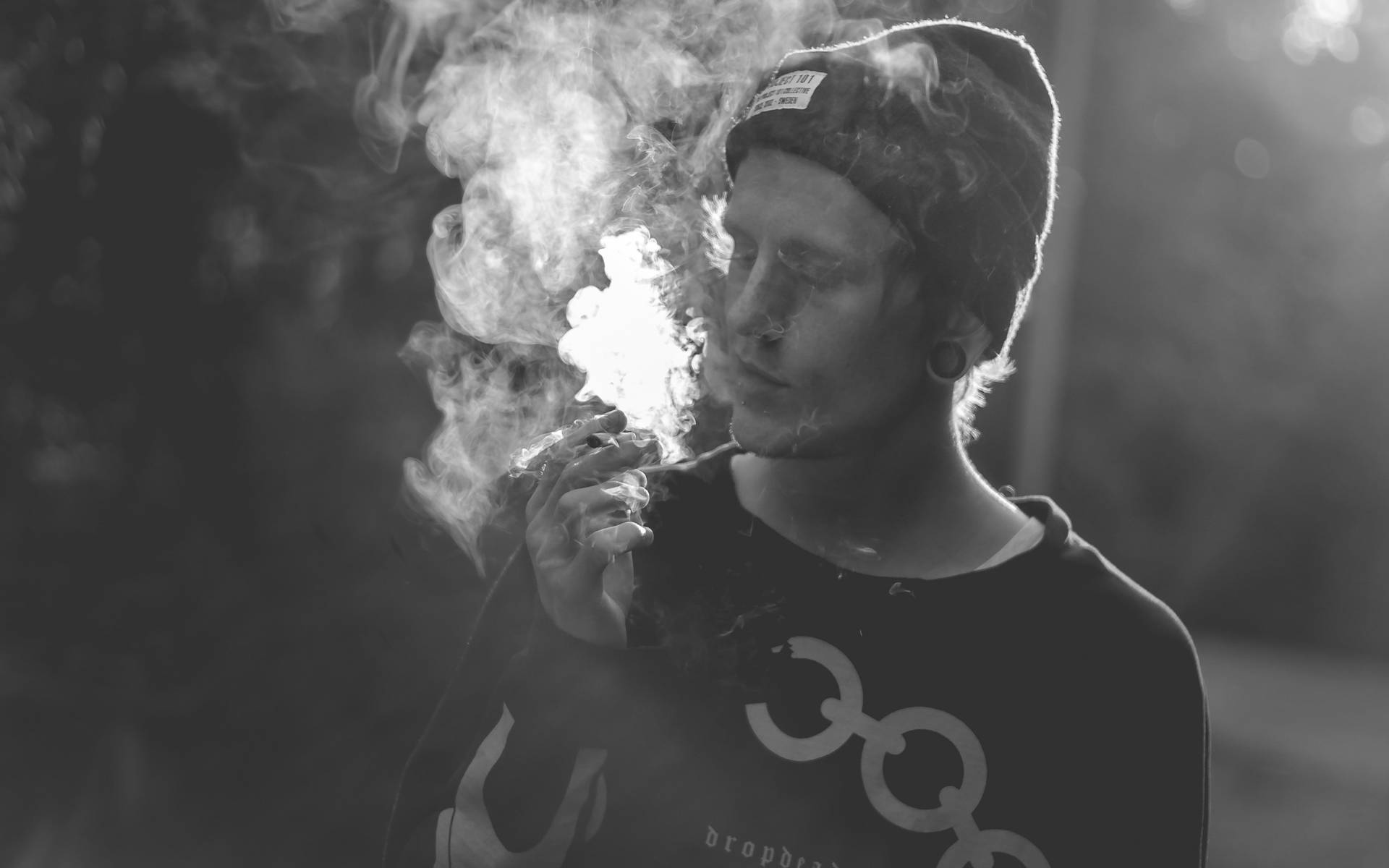 戴冷帽的人手持香煙在戶外呼出煙霧的黑白照片。
