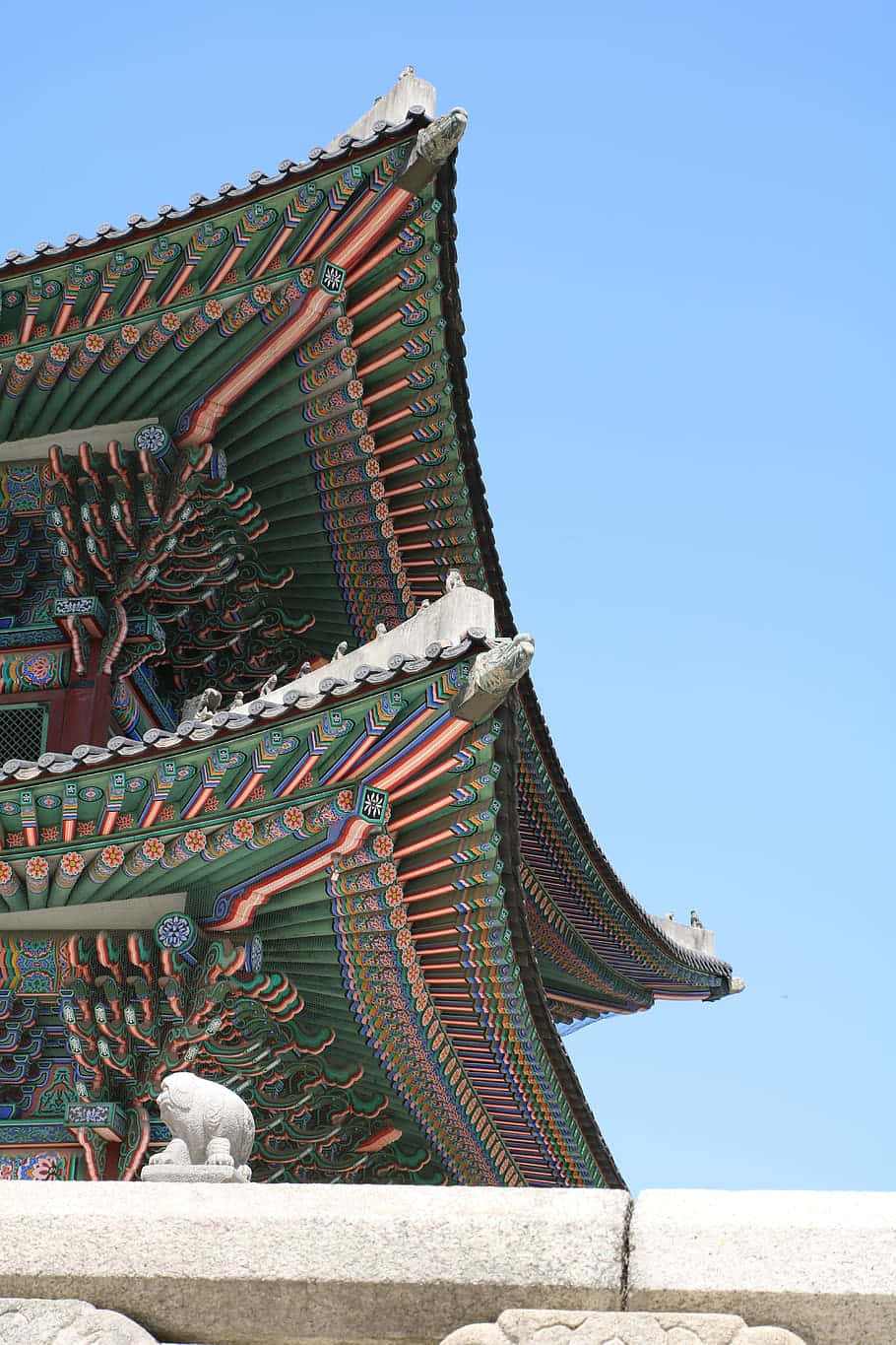 藍天下色彩繽紛的傳統韓國寺廟屋頂，帶有石獅雕像。