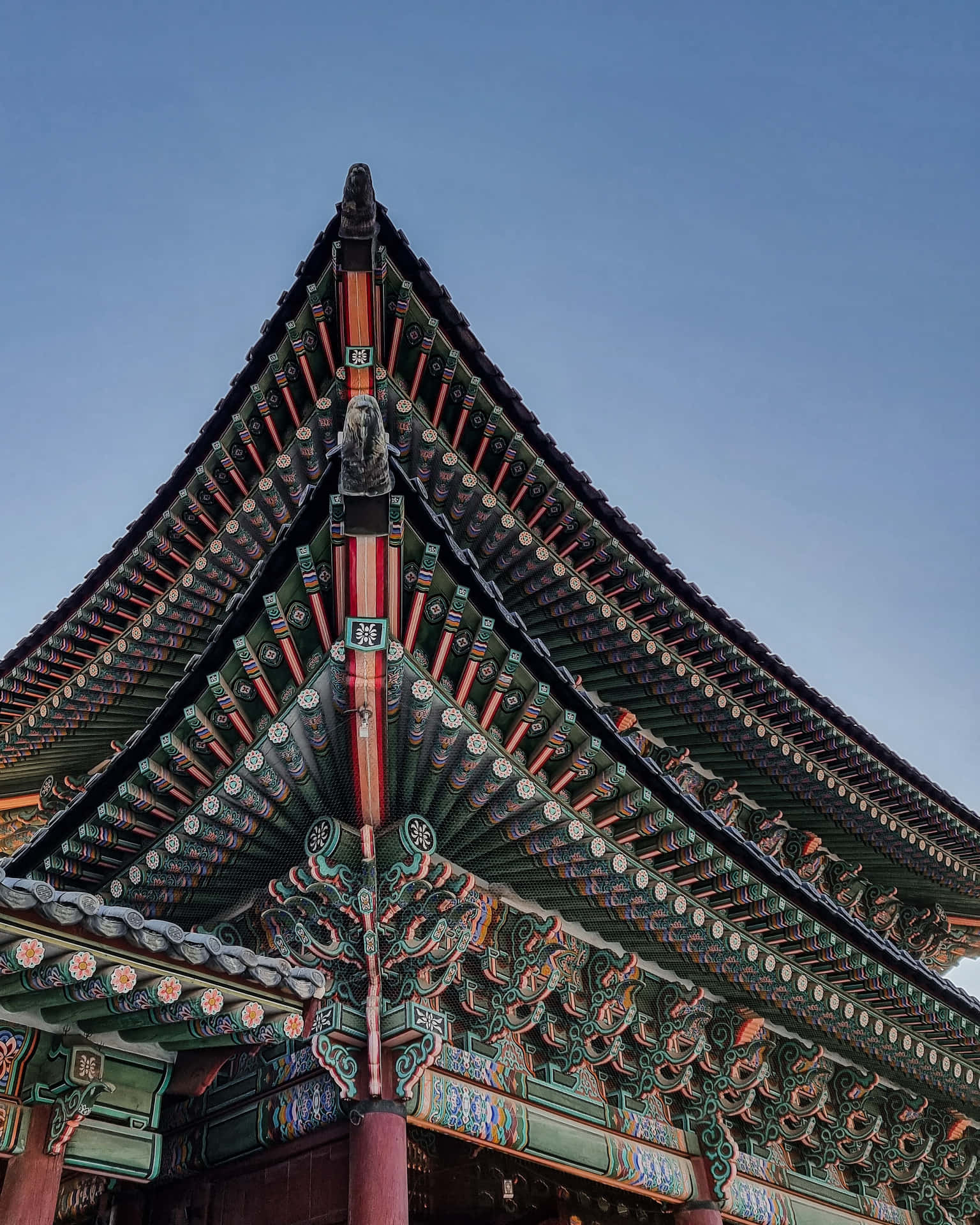 景福宮屋頂特寫 壁紙 — 低角度觀看裝飾華麗的傳統韓國寺廟屋頂，在清澈的藍天下呈現複雜的綠色、紅色和金色細節。