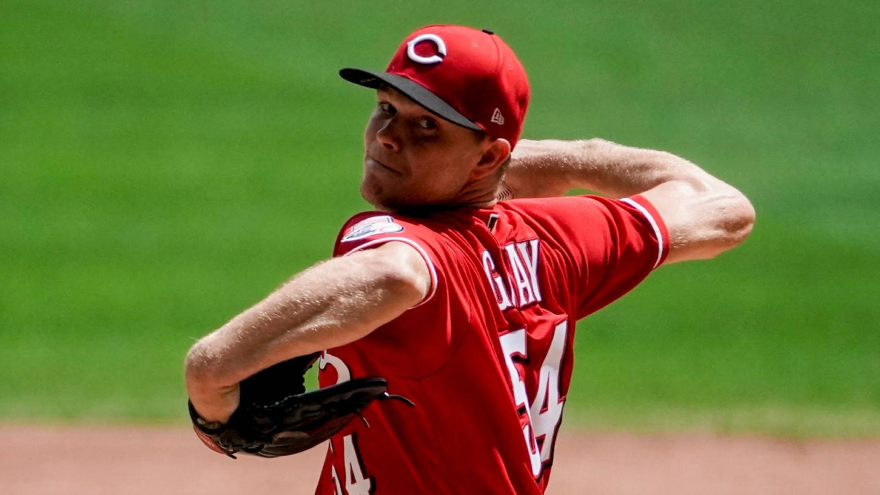 晴天下的 Sonny Gray 壁紙 — 身穿紅色球衣的棒球投手在綠色球場上專注地投球。