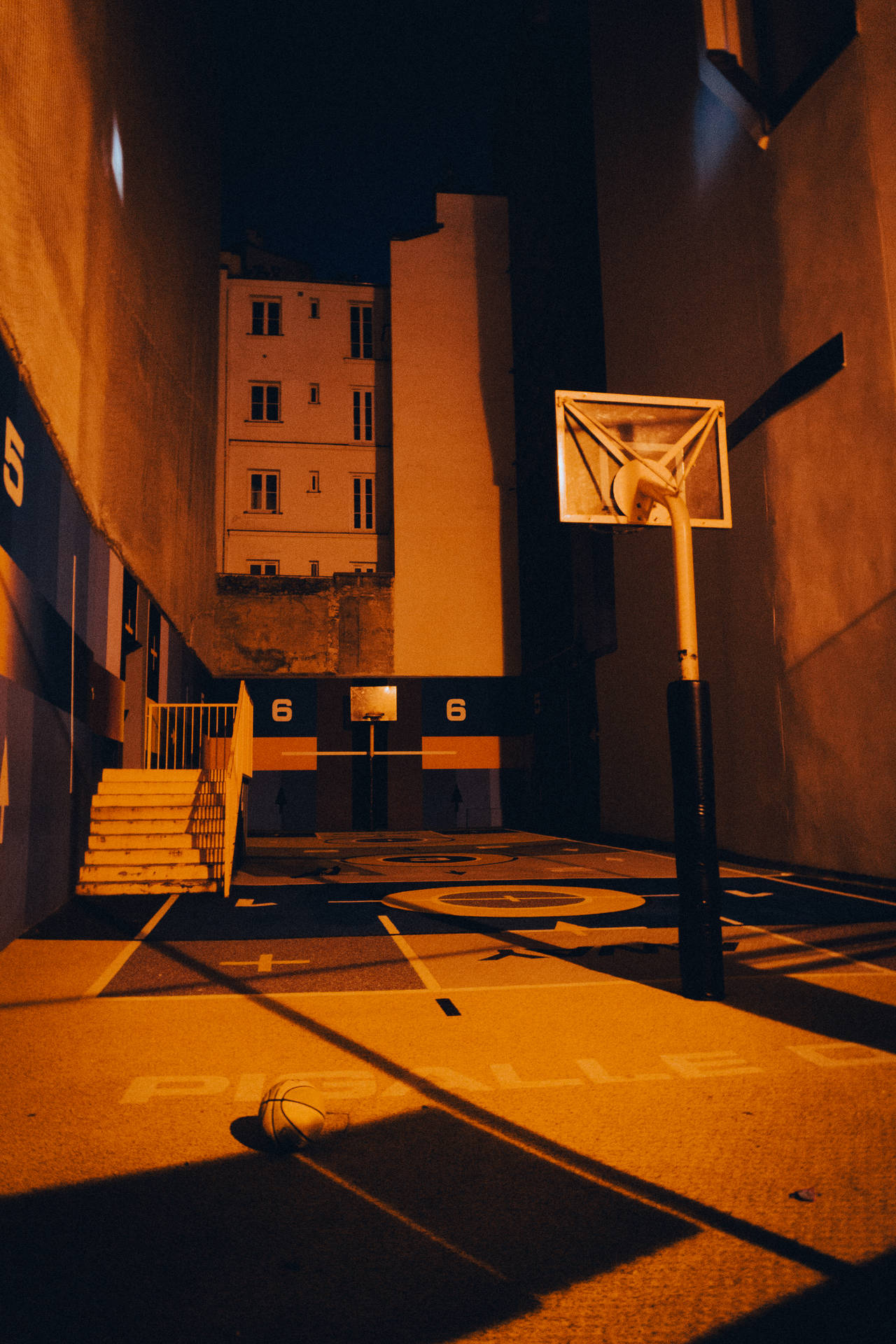 夜晚空無一人的籃球場，溫暖的燈光，地上有一個籃球。