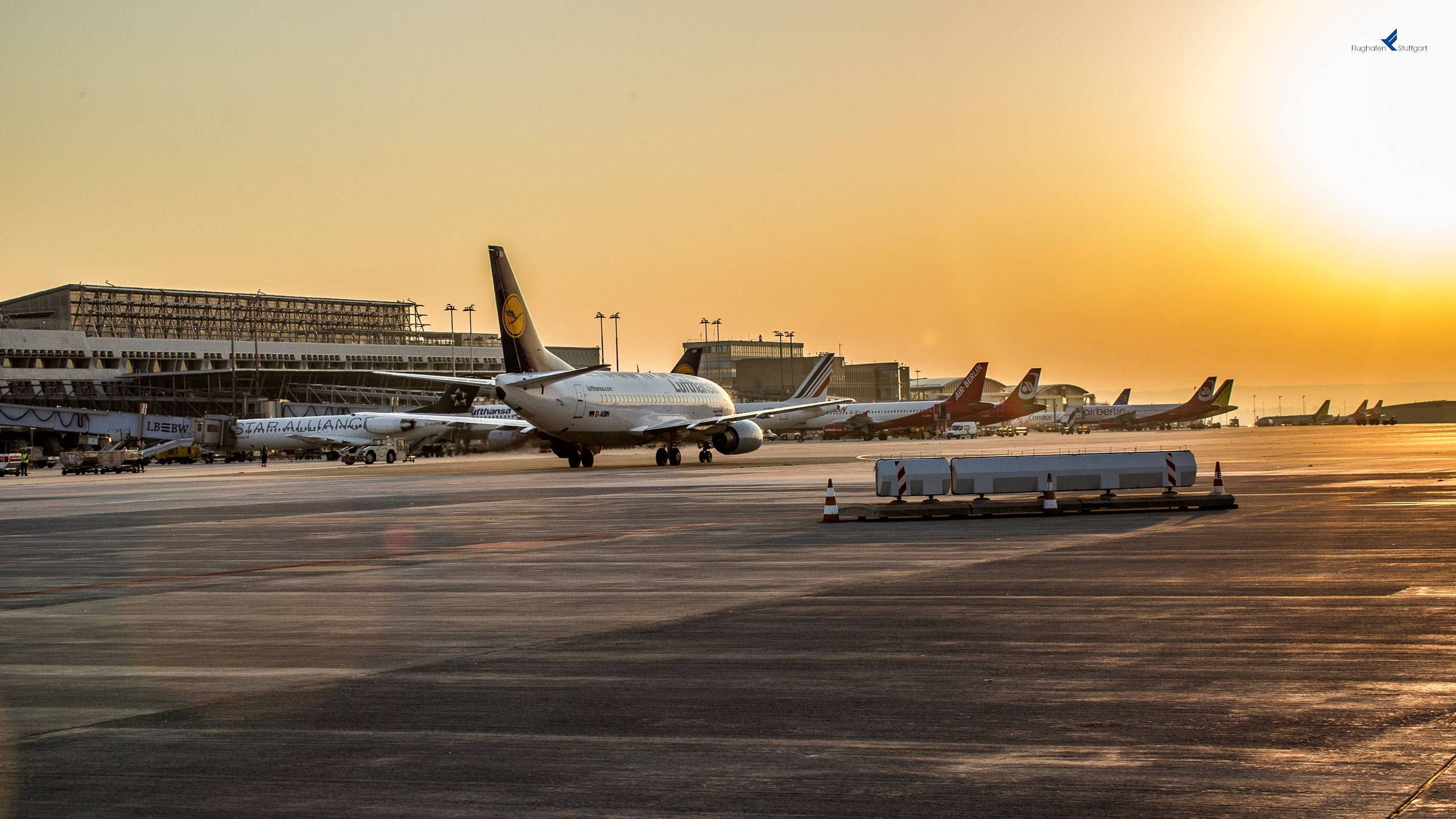 晴日機場風景 壁紙 — 金色夕陽以溫暖光線沐浴機場停機坪，飛機在閘口休息，背景是客運大樓。