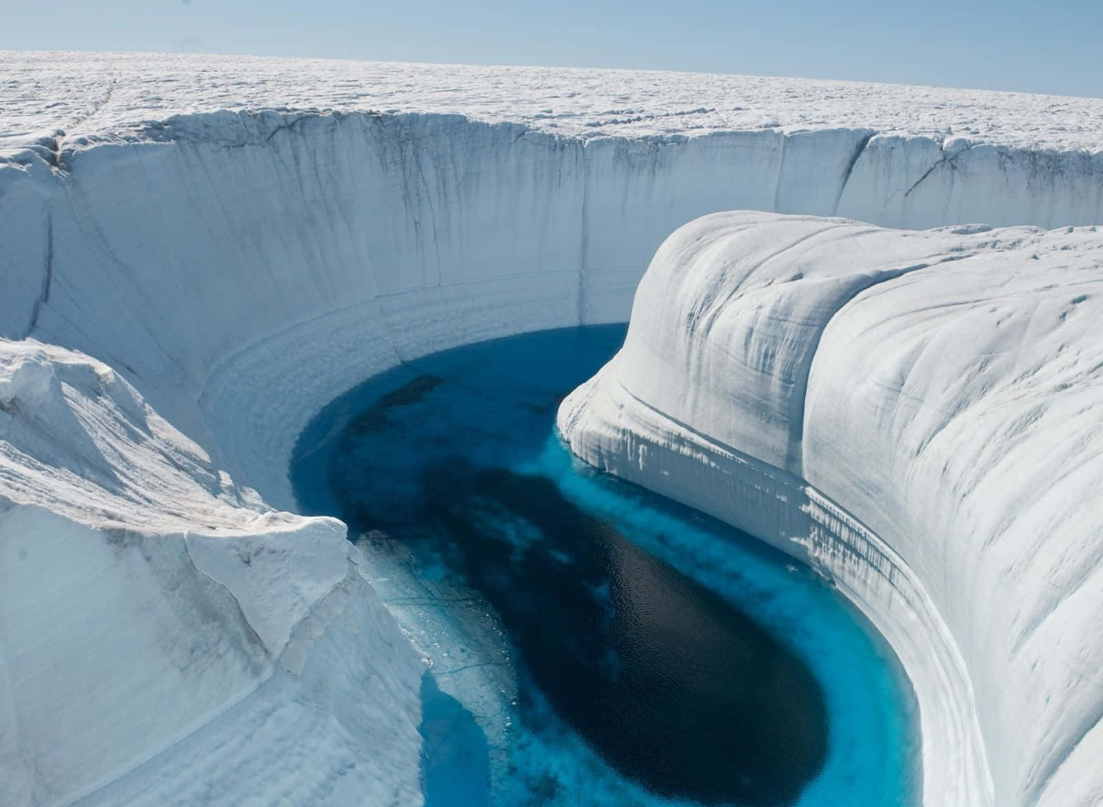Greenland 桌布 壁紙 — 晴朗天空下，深藍色融水池塘被純白積雪環繞的壯麗冰峽谷鳥瞰圖。