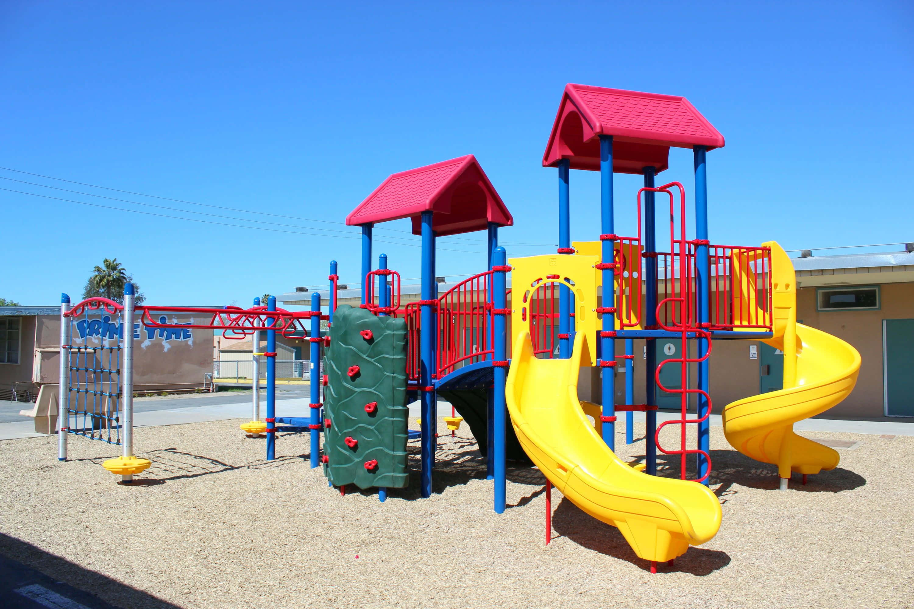 Playground 桌布 壁紙 — 晴朗日子裡，在清澈藍天下，充滿活力的遊樂場，有黃色滑梯、紅色屋頂和藍色結構。