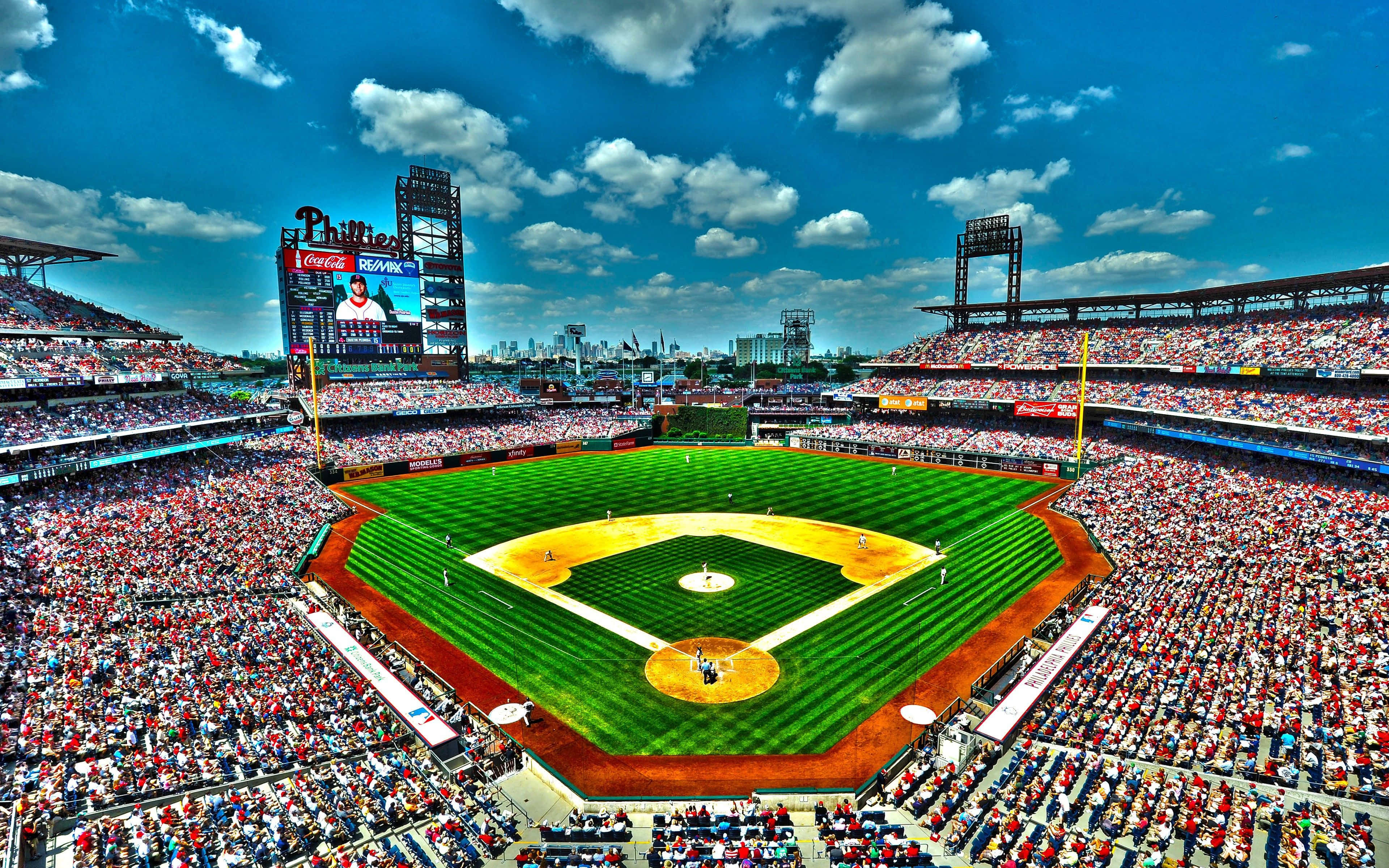 Baseball Stadium 桌布 壁紙 — 晴朗藍天白雲下，擠滿觀眾的棒球場鳥瞰圖。