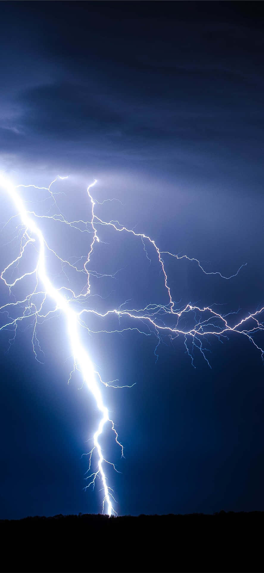 明亮的閃電照亮了剪影山丘上方黑暗的暴風雨天空。