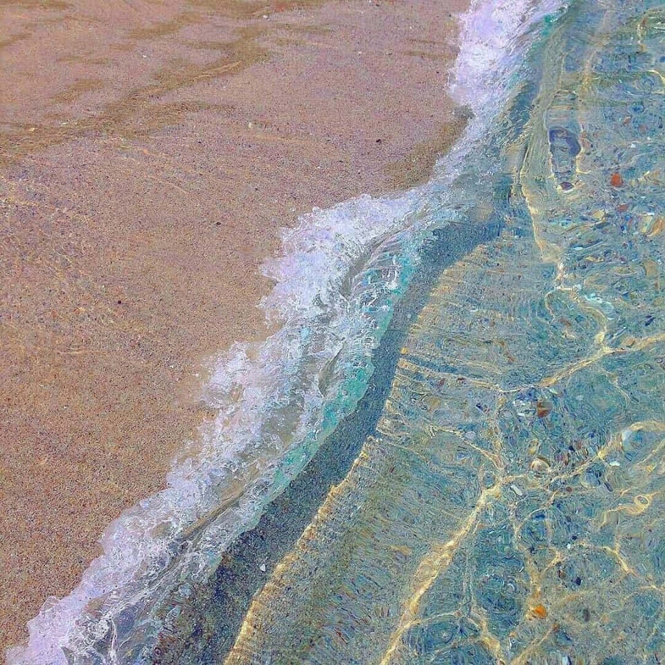 晶瑩藍海灘美學圖片 壁紙 — 溫柔的海浪沖刷金色沙灘的特寫，在清澈的碧綠海水下顯露出色彩繽紛的鵝卵石。