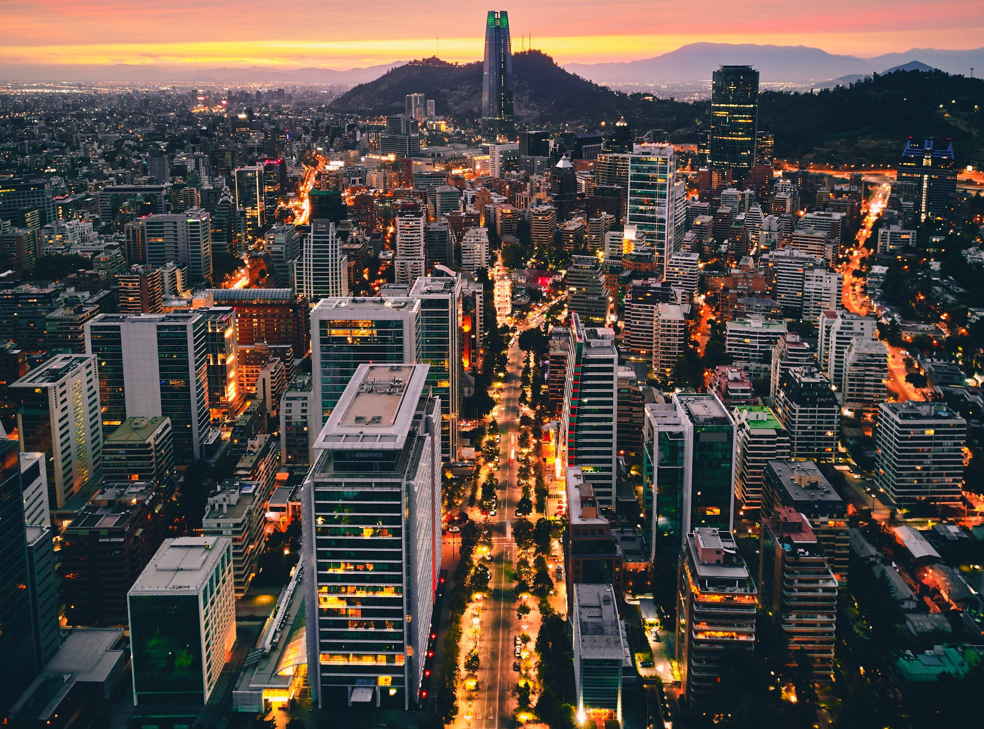 智利城市景觀 壁紙 — 黃昏時分，一座廣闊城市的鳥瞰圖，發光的街道和高聳的摩天大樓映襯著火紅的橙色天空。