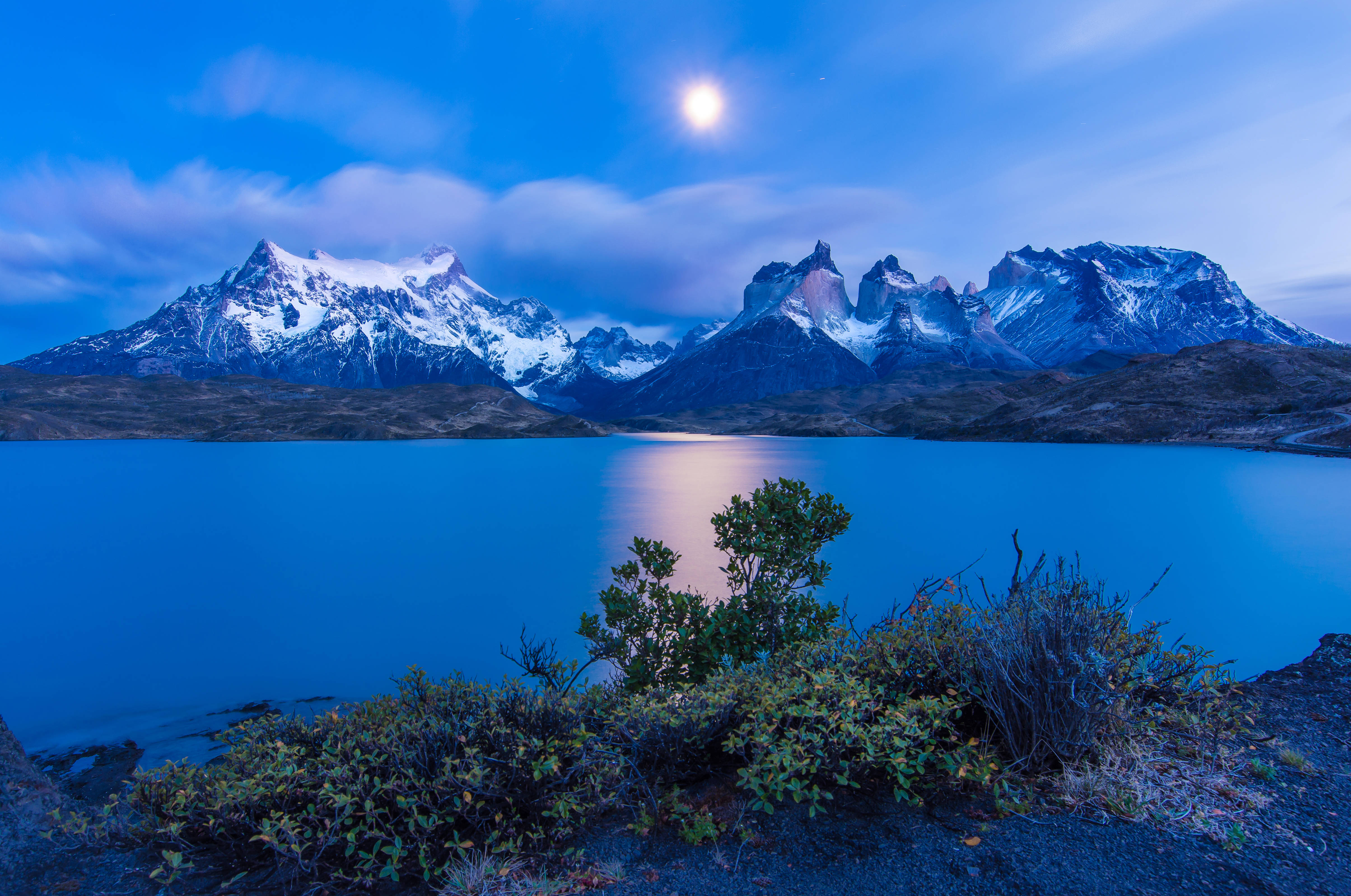 智利帕伊恩山脈夜景 壁紙 — 寧靜的月光湖面映照著在柔和的藍色暮色天空下，積雪覆蓋的山峰之上閃耀的月亮。