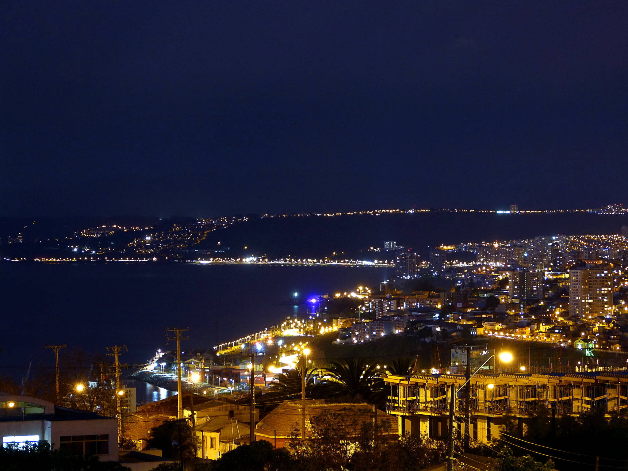 智利瓦爾帕萊索夜景 壁紙 — 沿海灣的 vibrant 夜間城市景觀，發光的街燈和建築物倒映在黑暗的水面上。