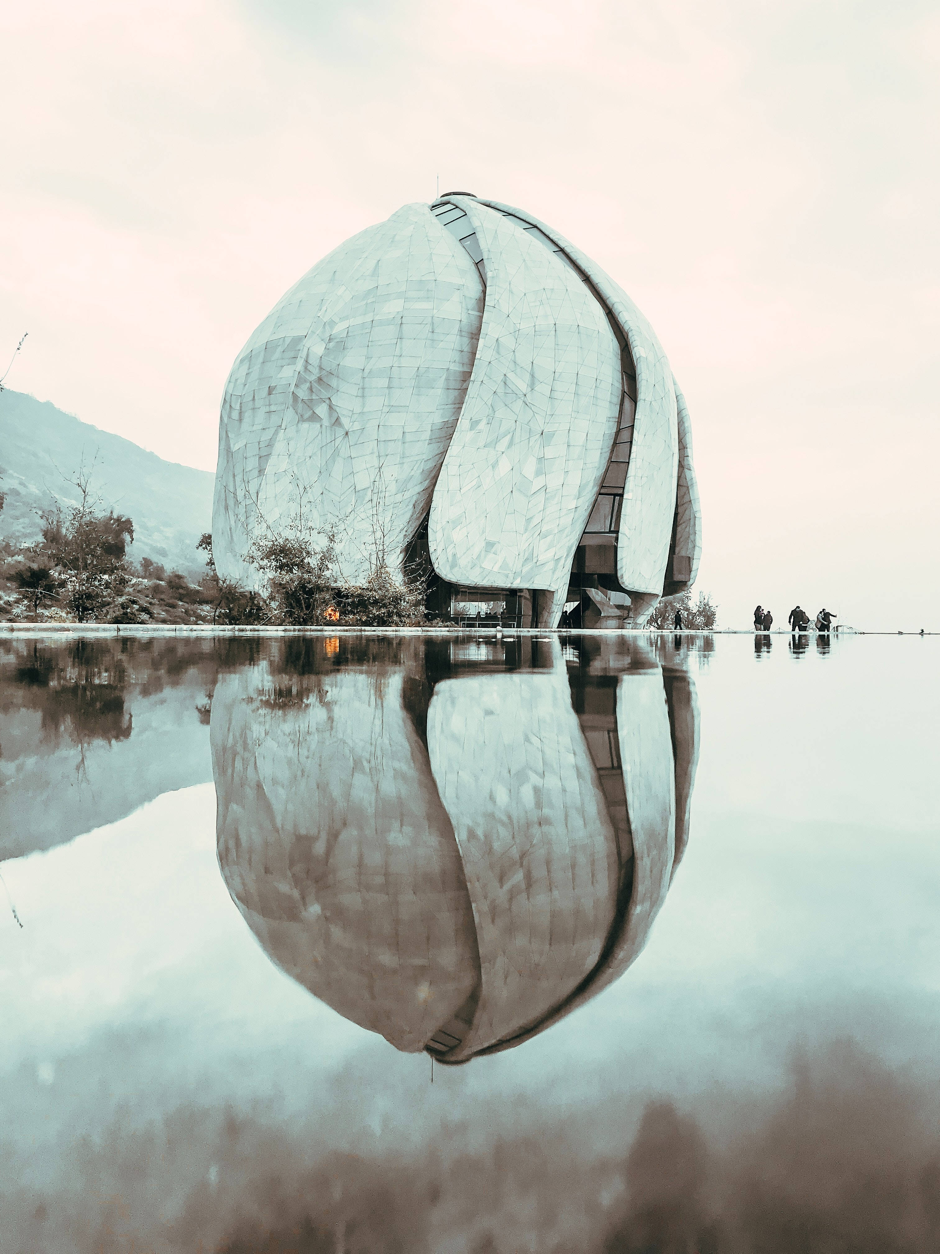 智利聖地亞哥巴哈伊教廟宇倒影 壁紙 — 一座未來主義的圓頂建築，帶有紋理金屬表面，完美倒映在陰天下一片平靜淺水之中。