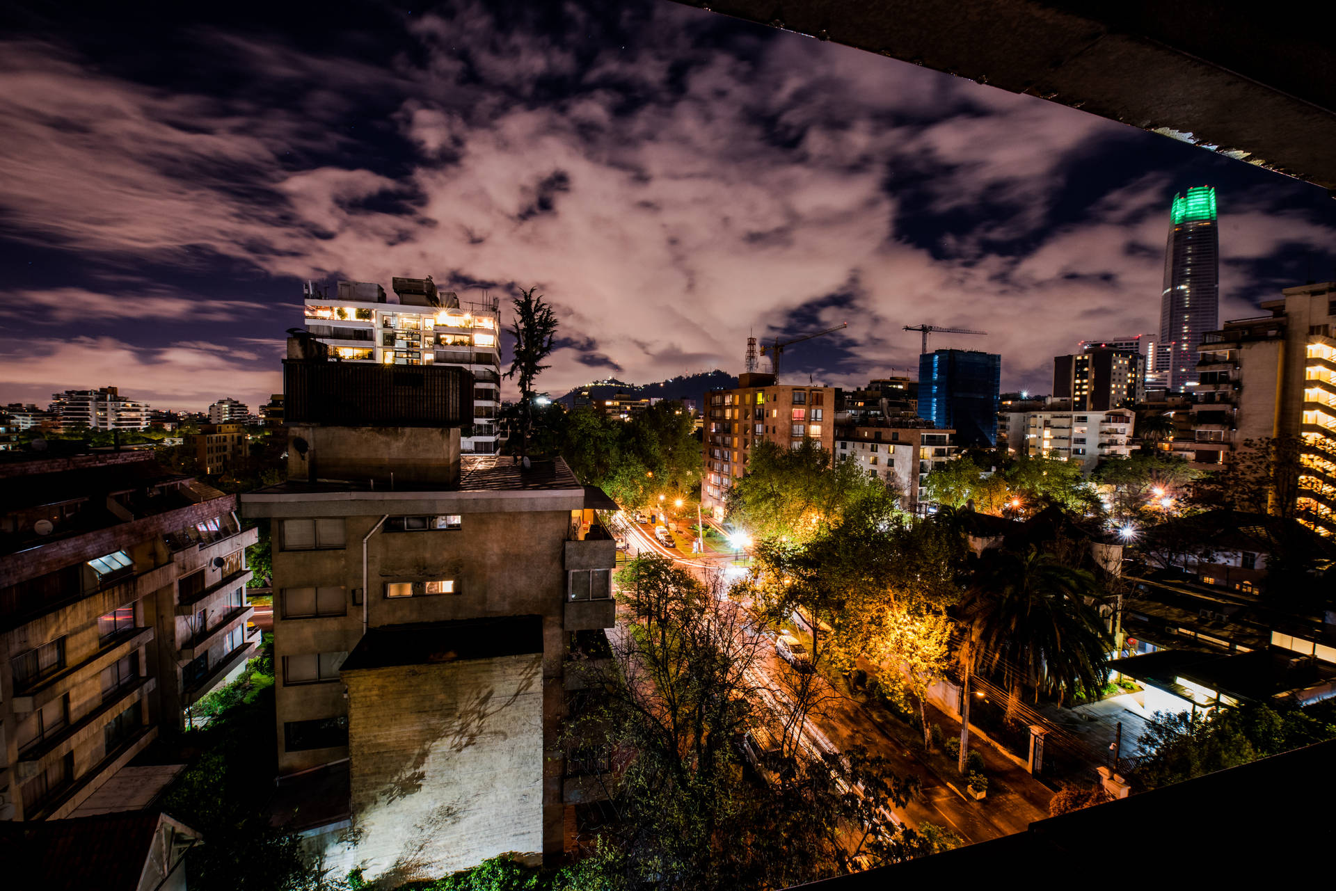 智利聖地亞哥美學夜空 壁紙 — 在戲劇性的多雲天空下，充滿活力的夜景，有照明建築物和發光的街燈。