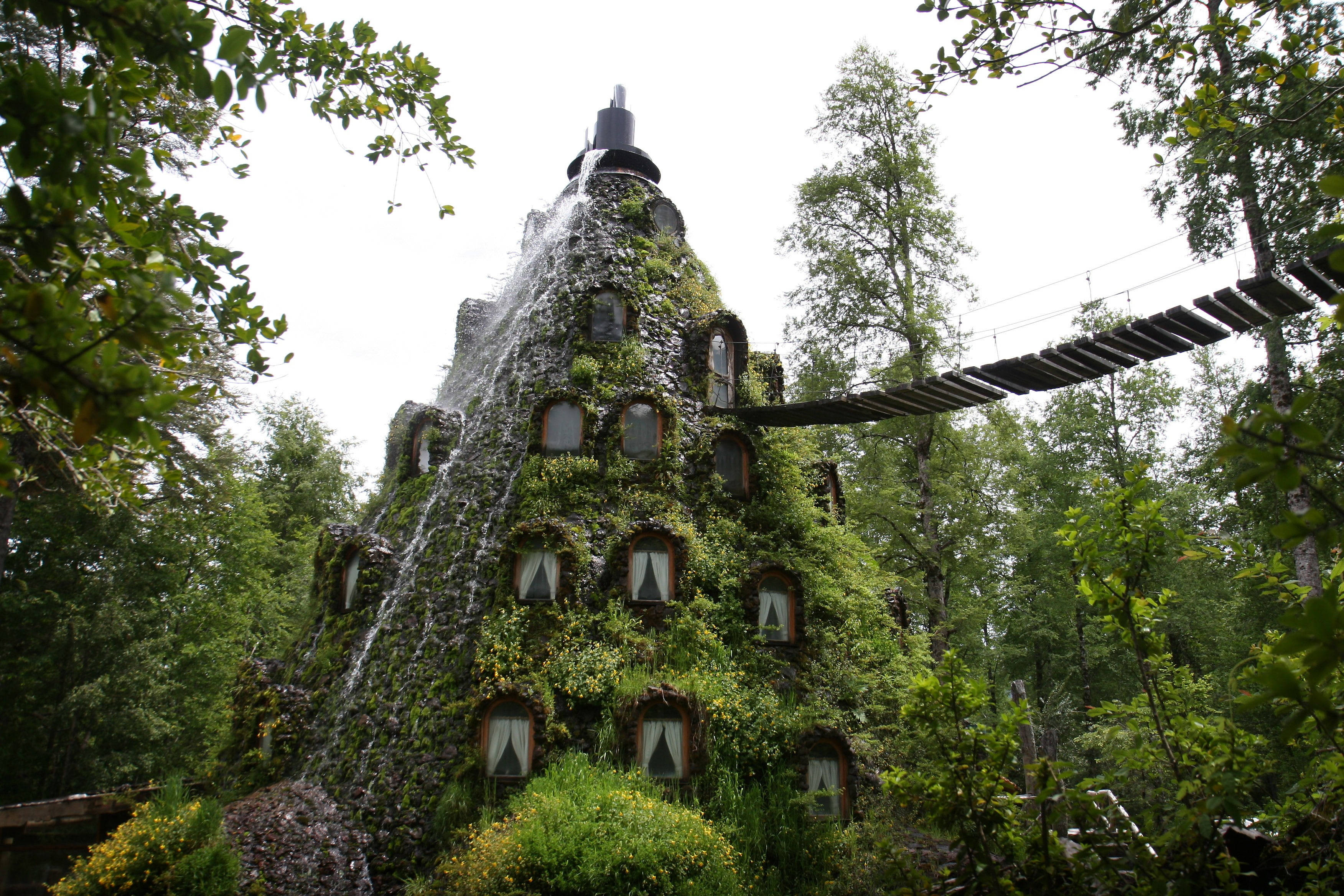 智利蒙塔尼亞馬吉卡旅館 壁紙 — 一座長滿青苔的圓錐形建築，瀑布傾瀉而下，木橋橫跨其間，坐落在茂密的綠色森林中。