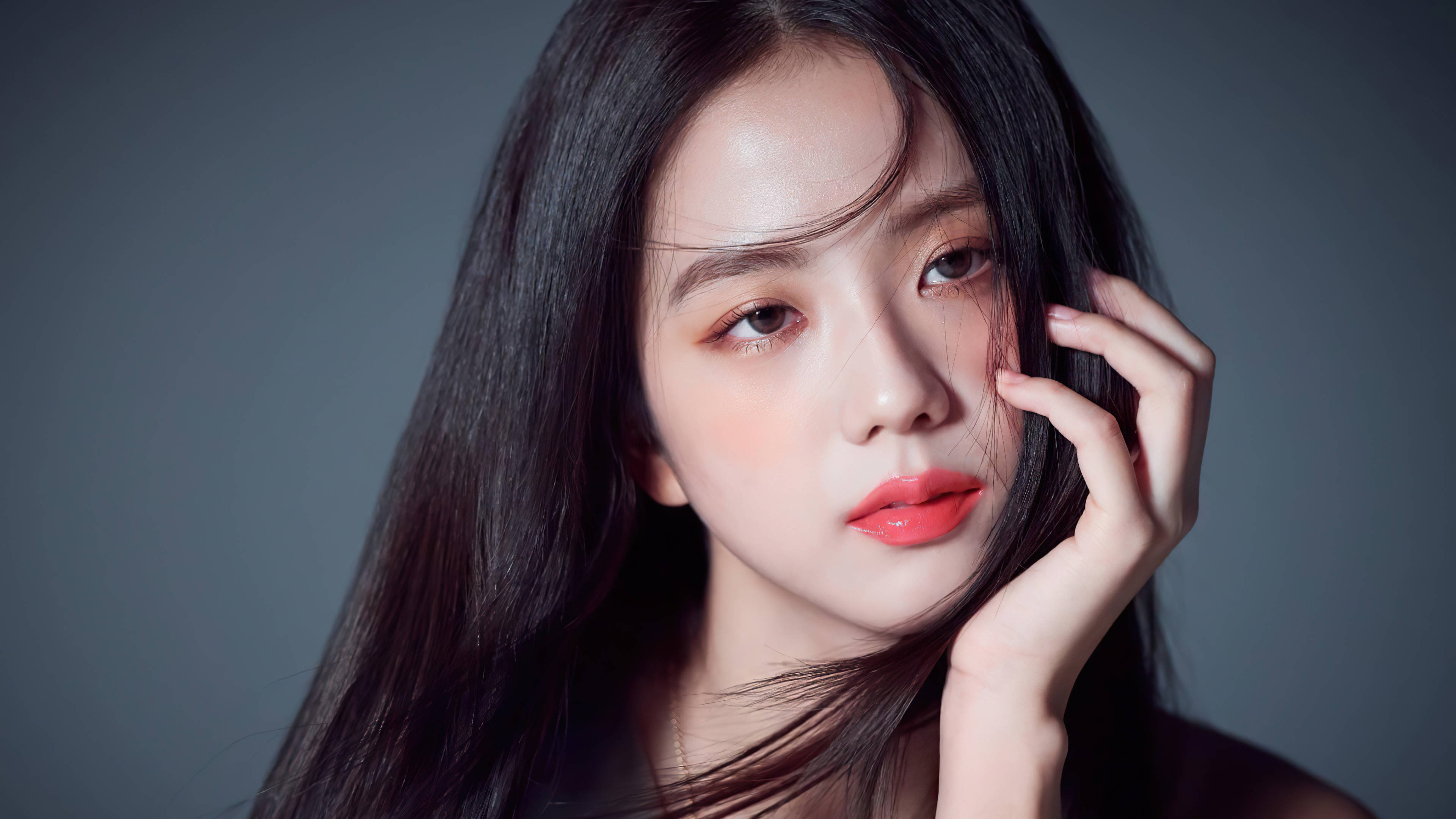 智秀 Vogue 韓國版寫真 壁紙 — 一位長黑髮、紅唇大膽的年輕女性，輕輕將臉頰貼在柔和的灰色背景上。