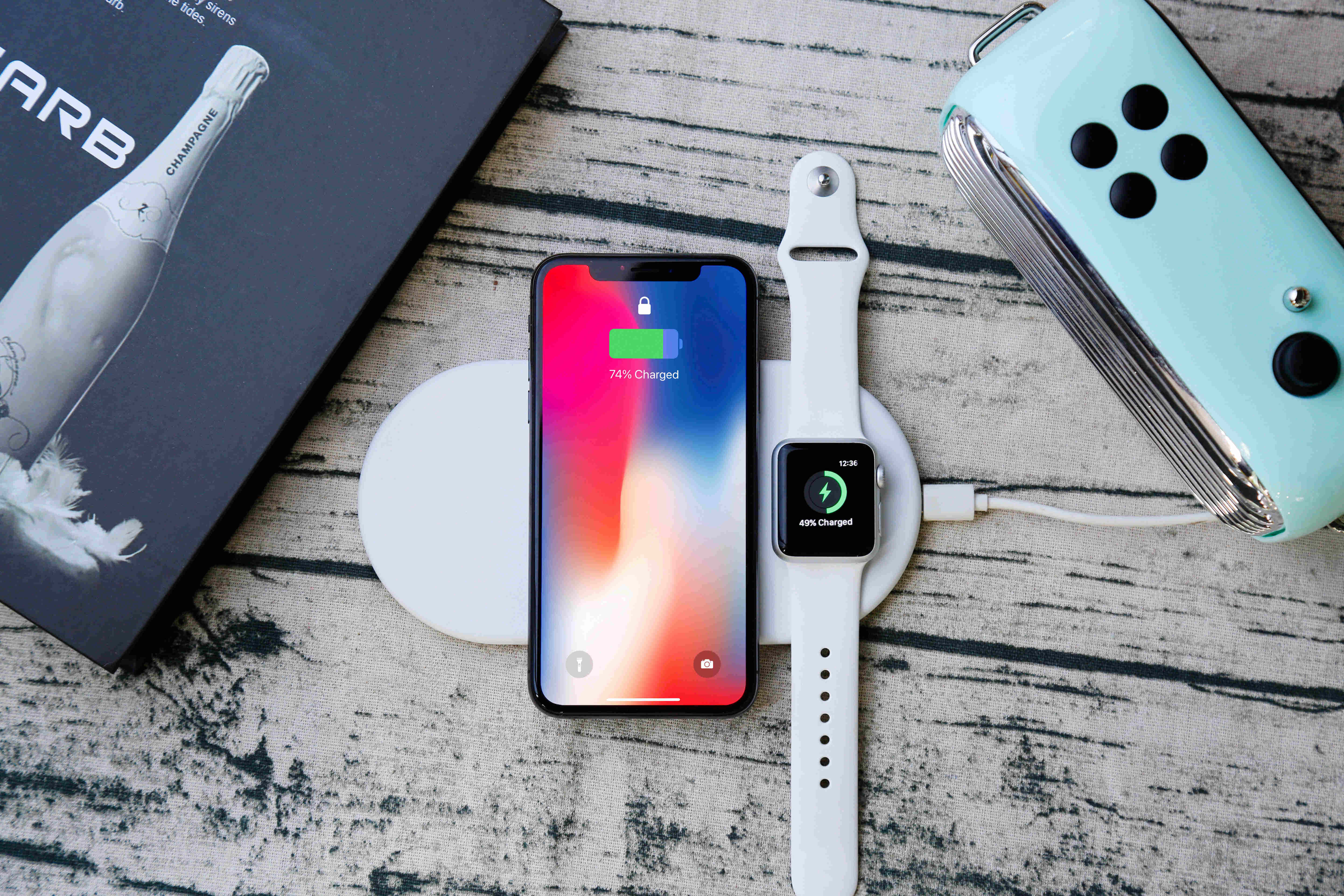 Wireless Charging 桌布 壁紙 — 智能手機和智能手錶在白色充電板上無線充電，旁邊是薄荷色控制台和香檳書，置於風化木上。
