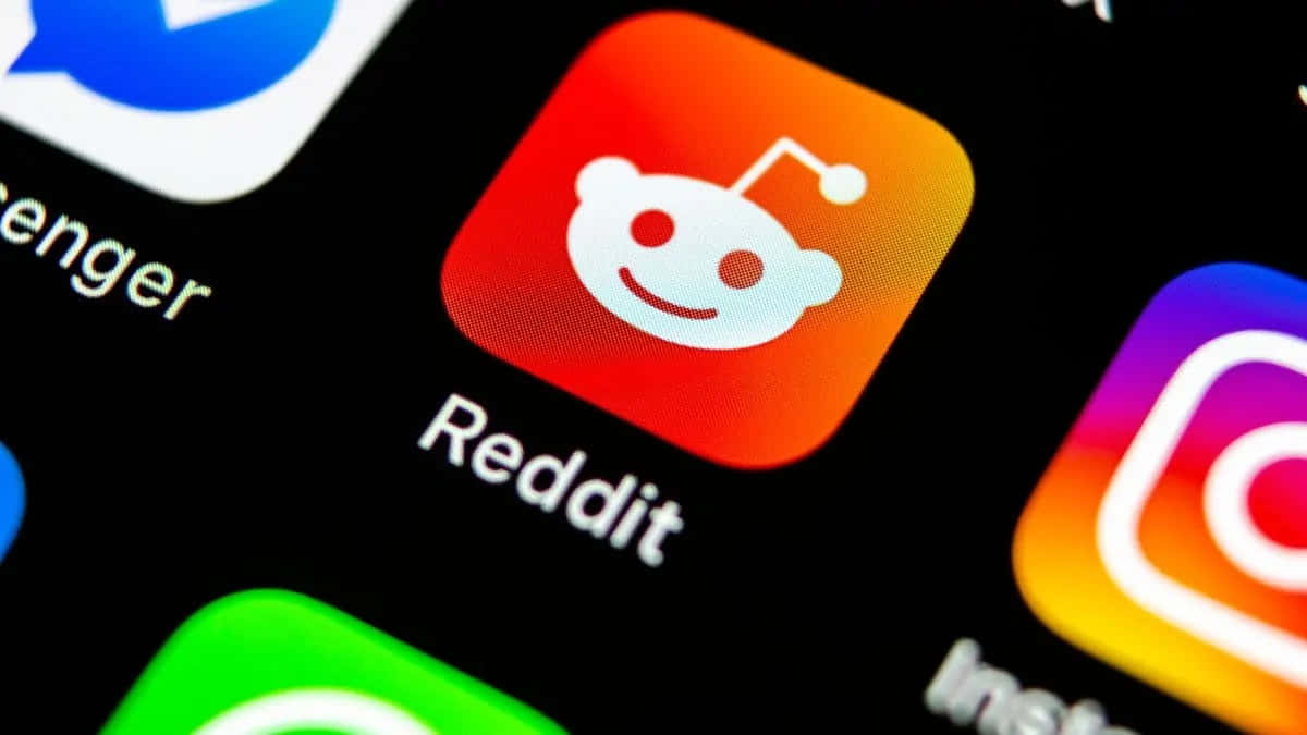 reddit 桌布 壁紙 — 智能手機屏幕特寫，顯示Reddit應用程式圖標在黑色背景上發出紅橙色漸變光芒。