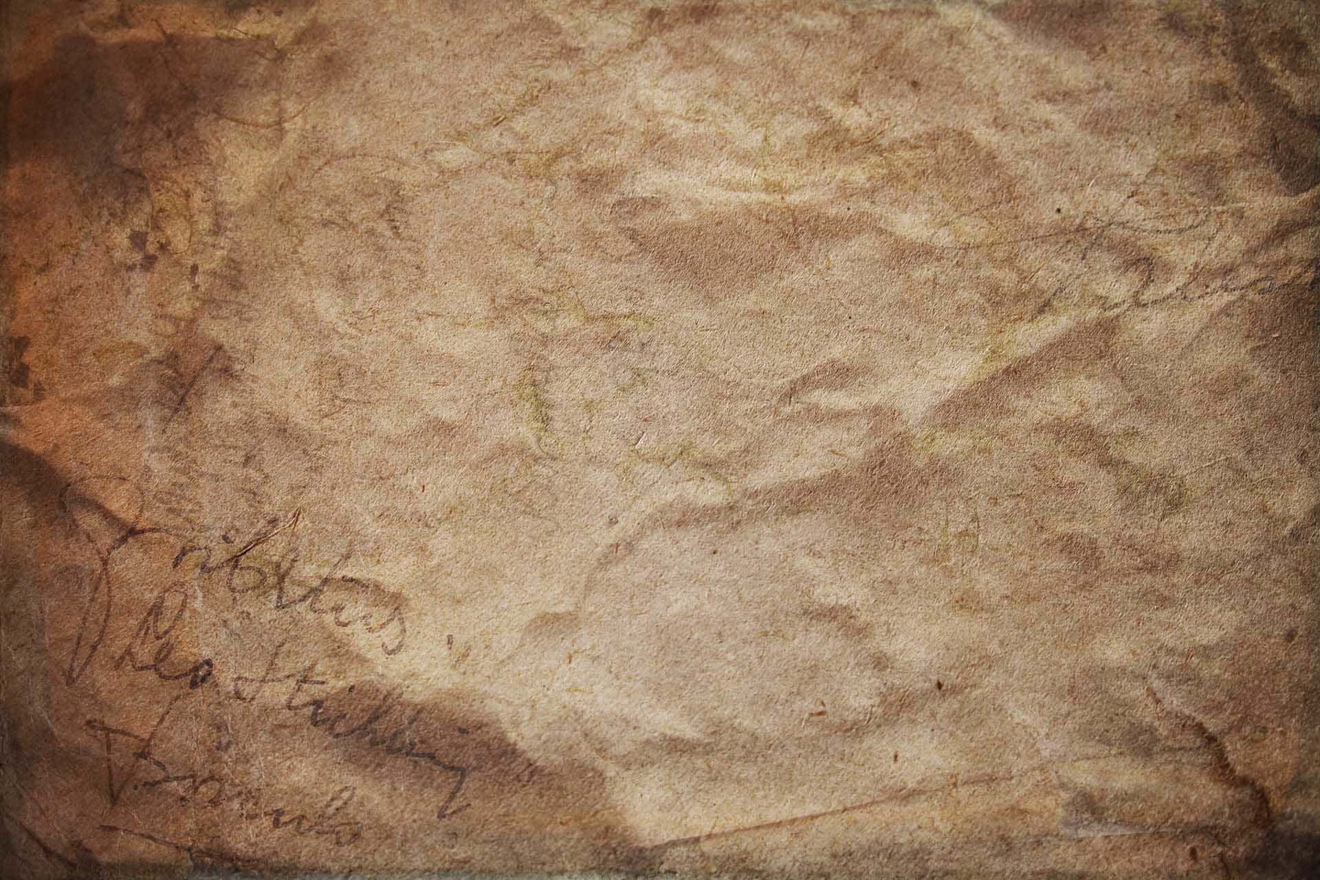 Brown Vintage 桌布 壁紙 — 暖色燈光下，舊羊皮紙的特寫，帶有褪色的草書字體和可見的摺痕。