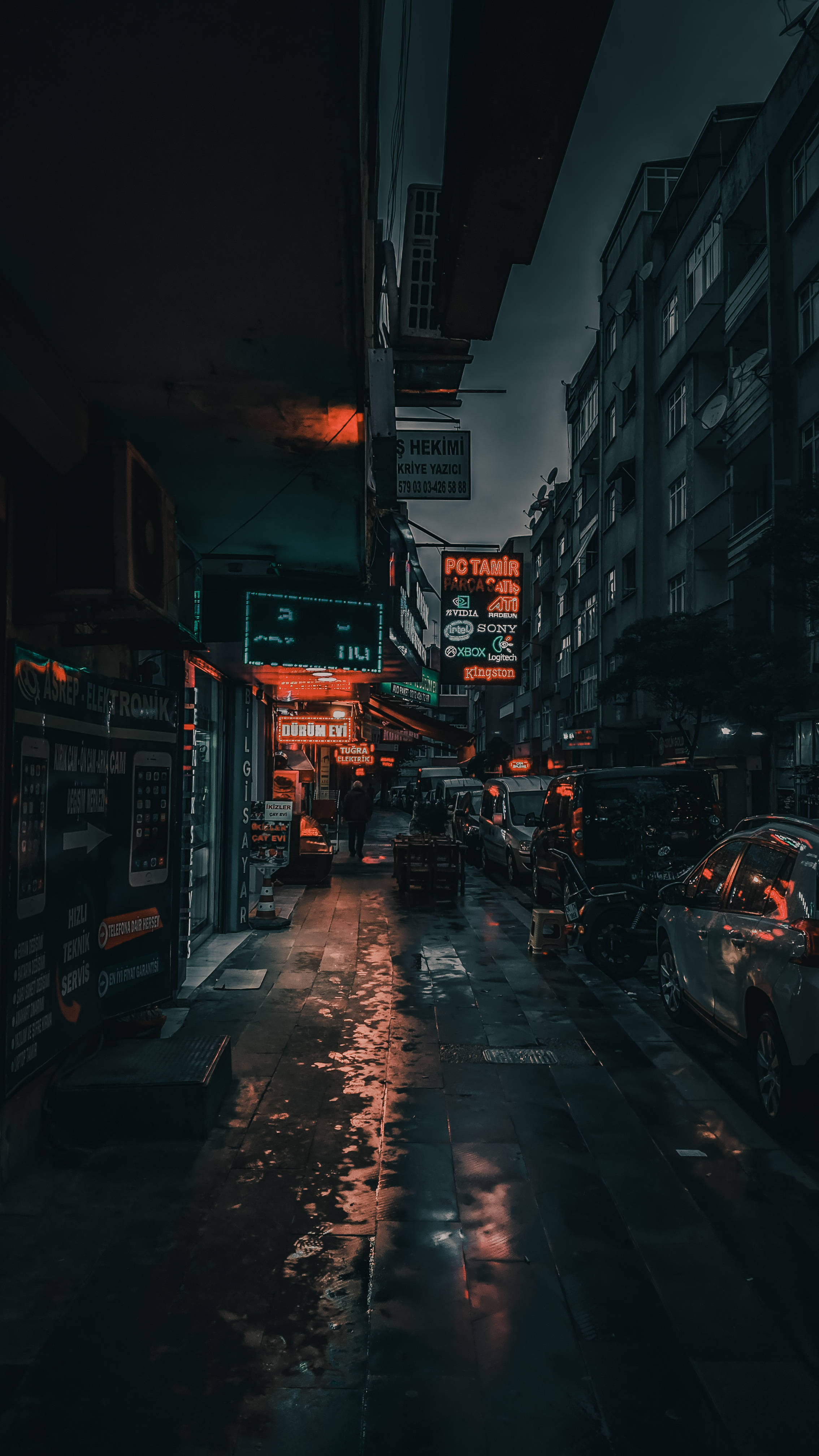 暗城街燈 壁紙 — 一條狹窄潮濕的城市小巷，夜晚被發光的霓虹燈招牌照亮，倒影映在濕漉漉的路面上。