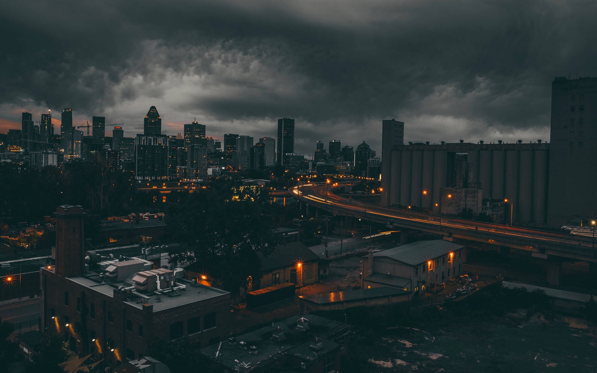 黑暗的暴風雲籠罩著城市景觀，閃爍的路燈和黃昏時分飛馳的車頭燈。 — 暗夜城市 壁紙