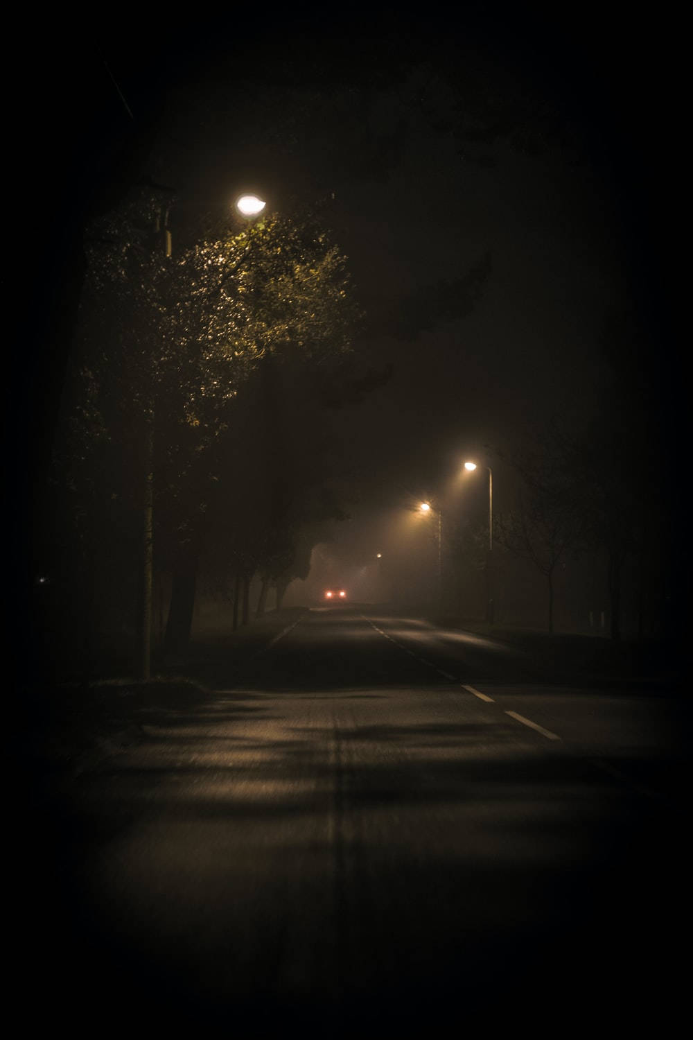 霧氣瀰漫的夜晚道路，由街燈照亮，遠處有汽車的車頭燈。