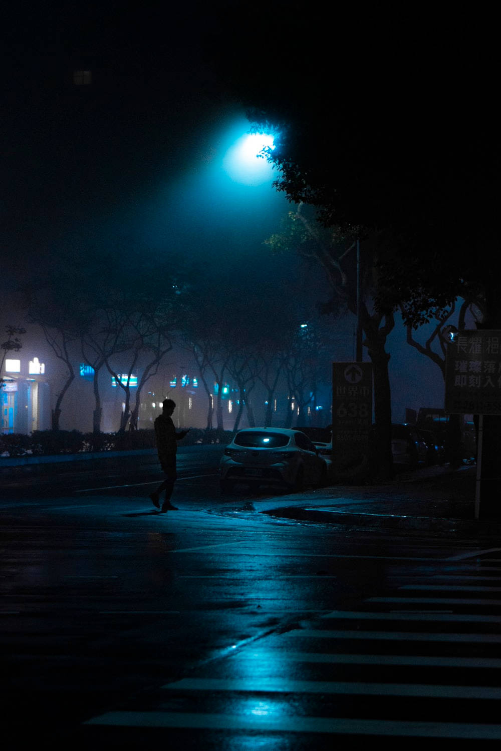 夜晚藍色街燈下，一個人影穿過濕漉漉的街道的剪影。