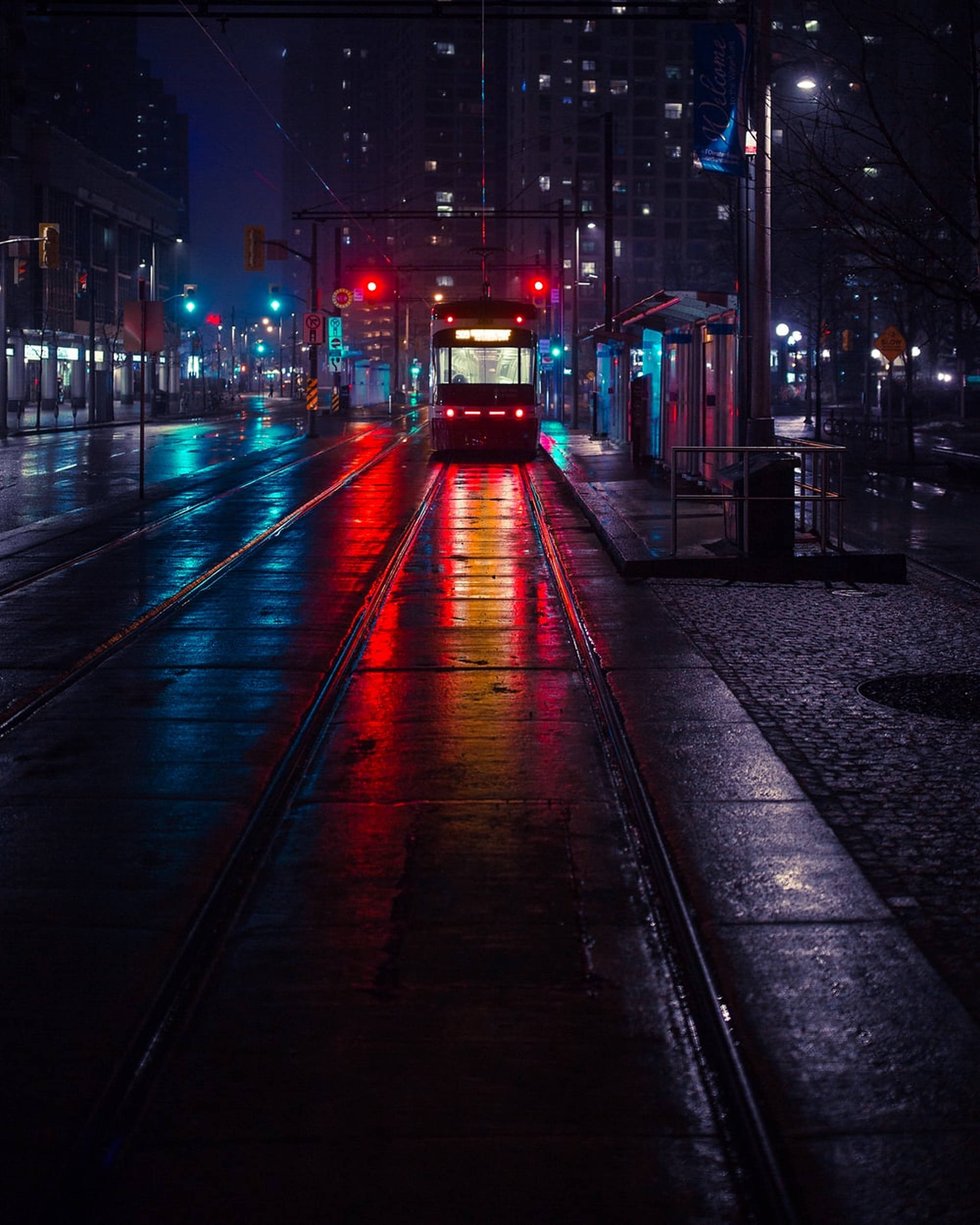 暗夜都市中的神秘鐵路 壁紙 — 雨濕的夜晚城市街道反射著電車和交通信號燈的紅色和藍色霓虹燈光。