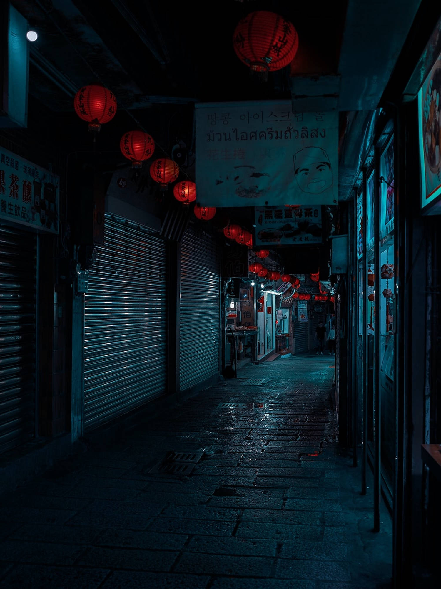 暗夜都市市中心 壁紙 — 夜晚一條狹窄潮濕的小巷，被發光的紅燈籠和霓虹燈招牌照亮，倒影在潮濕的路面上。