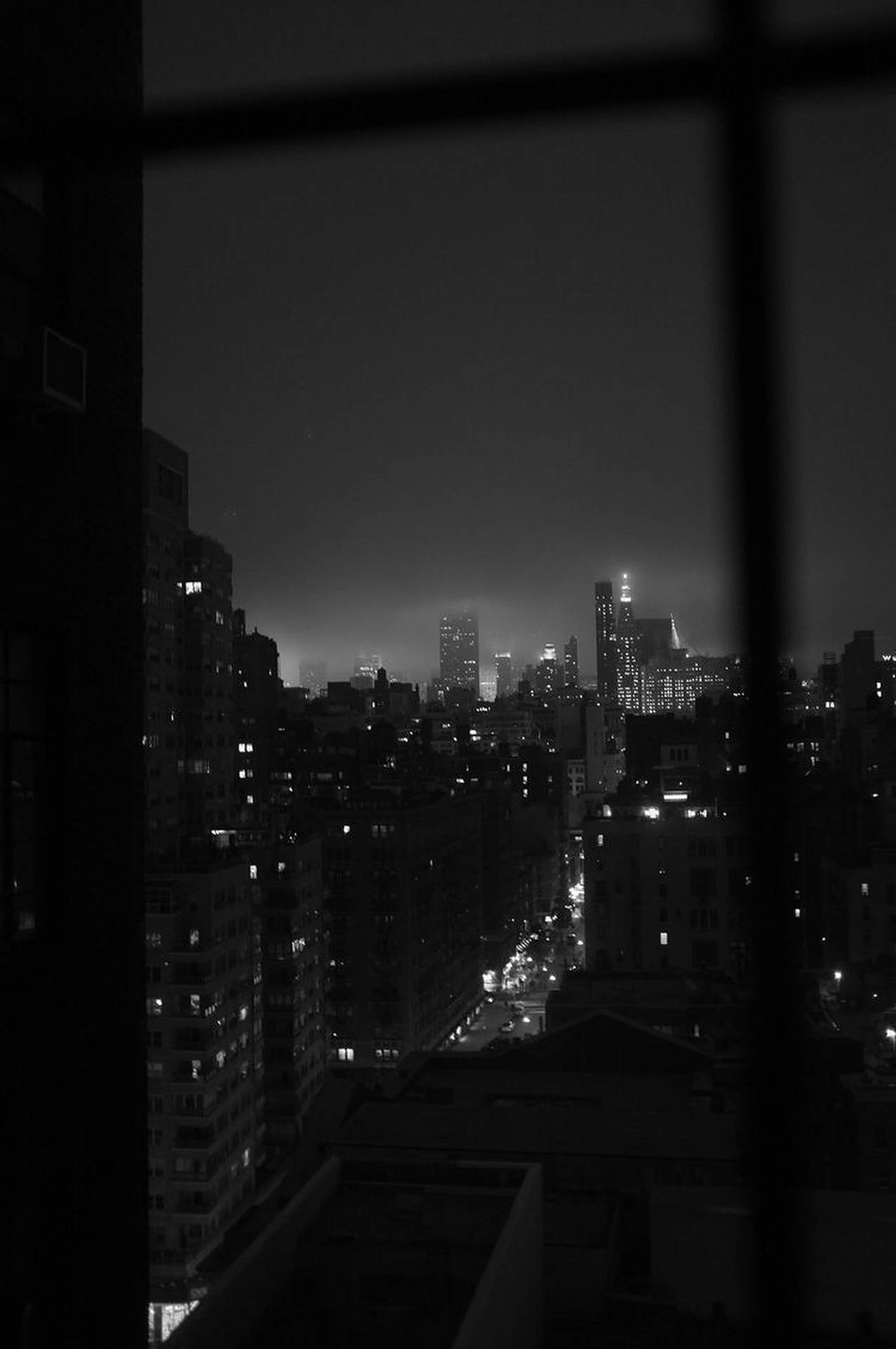 透過窗欄看到的夜景城市景觀，帶有發光的燈光。 — 暗夜城市 壁紙